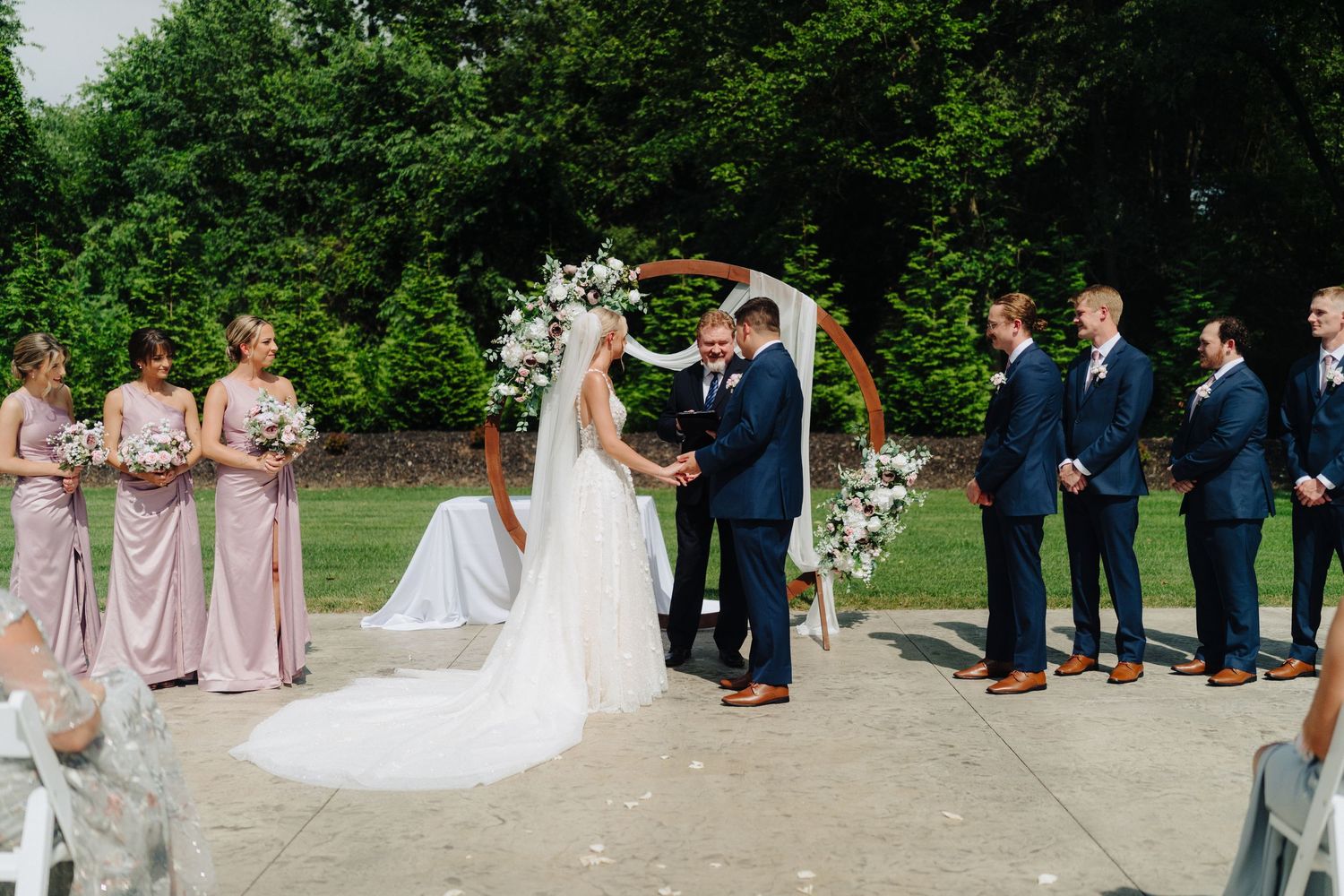 Wedding party in navy and blush colors gathered outdoors for ceremony photos.