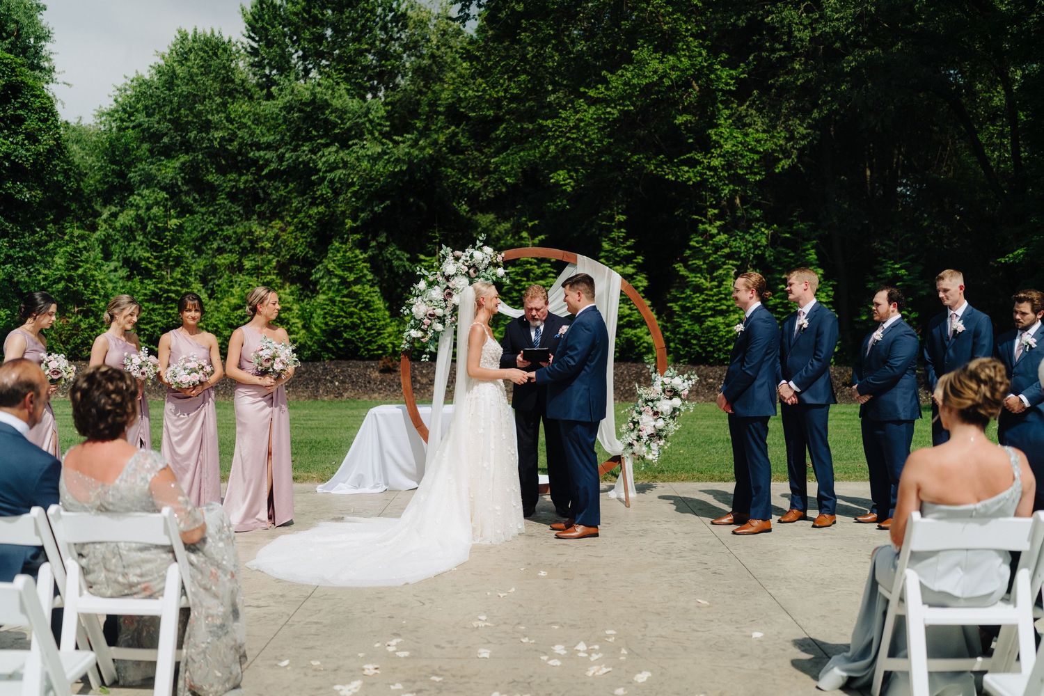 Wedding ceremony guests gather outdoors under trees for a celebration.