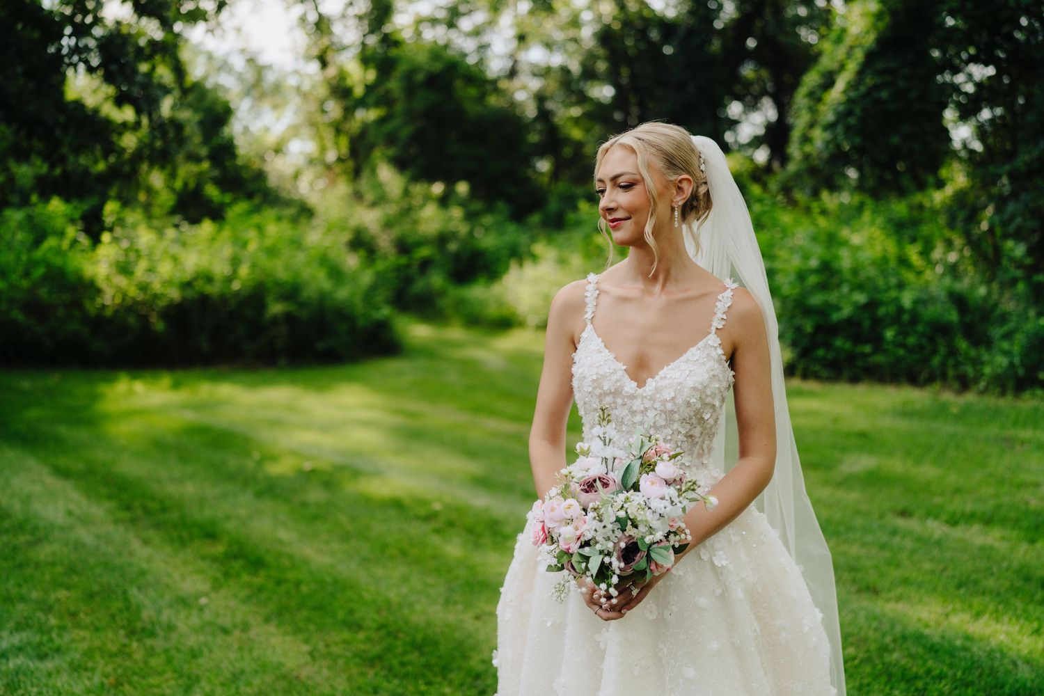 Bride in lace wedding dress holding bouquet in garden setting.