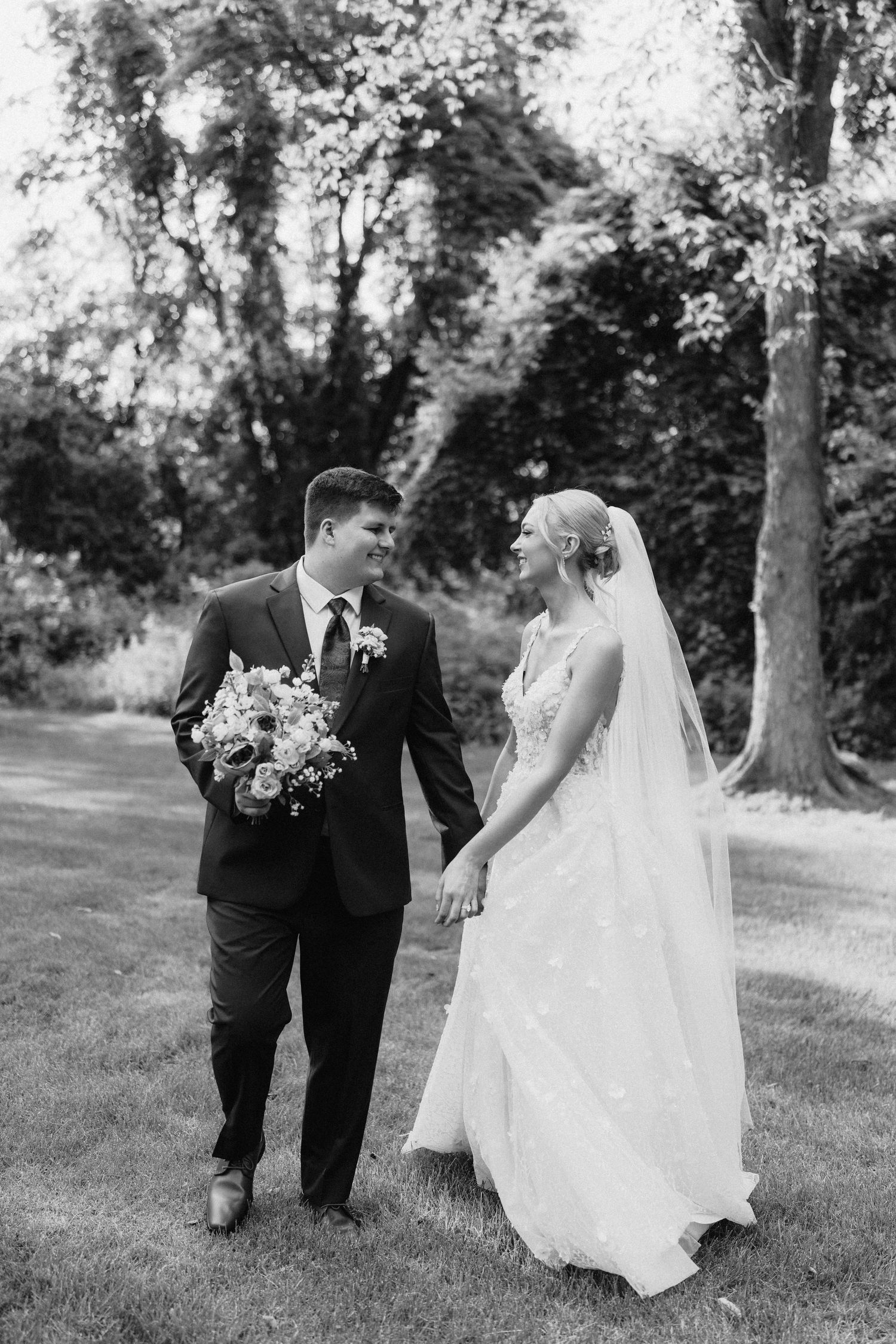 A romantic black and white photo series captures newlyweds walking together through a garden setting.