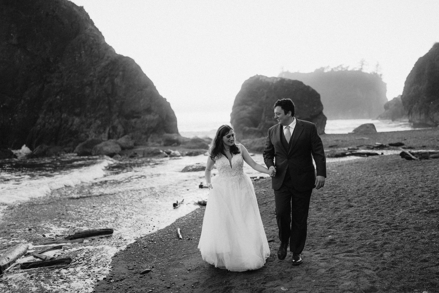 A black and white beach wedding photo with dramatic coastal rock formations in the background.
