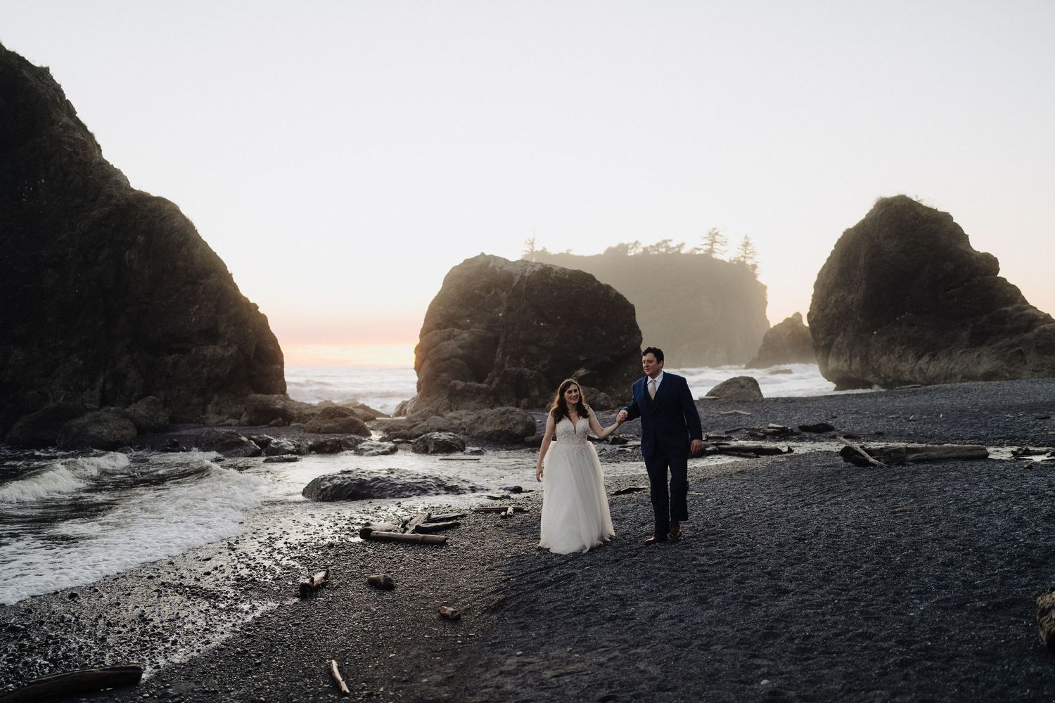 Dramatic coastal wedding photography with rocky cliffs and ocean waves at sunset.