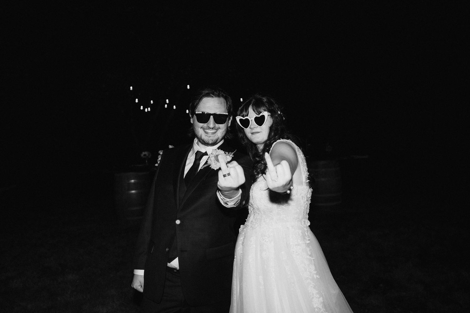 A black and white photo of a bride and groom wearing sunglasses at night while posing together.