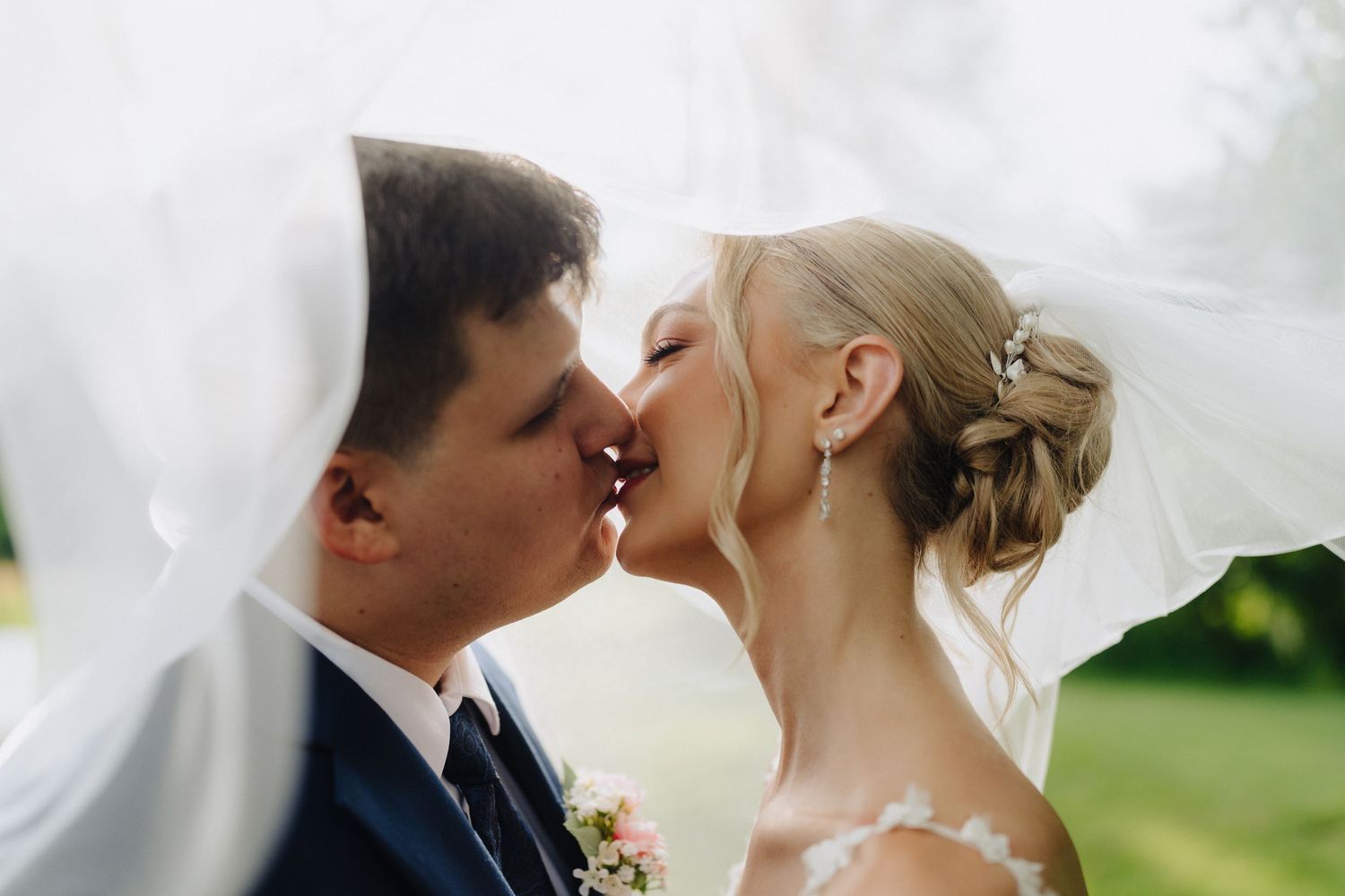 Romantic wedding couple shares intimate moment under flowing veil outdoors.