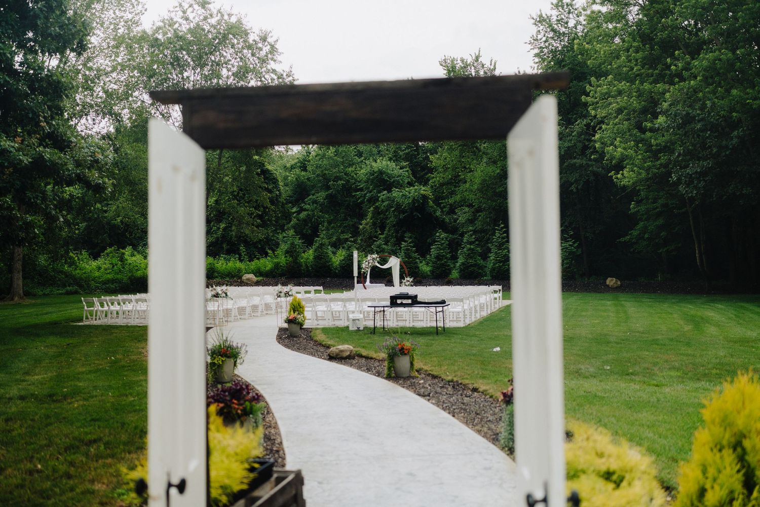 Outdoor wedding venue with white columns and pathway surrounded by lush green landscaping.