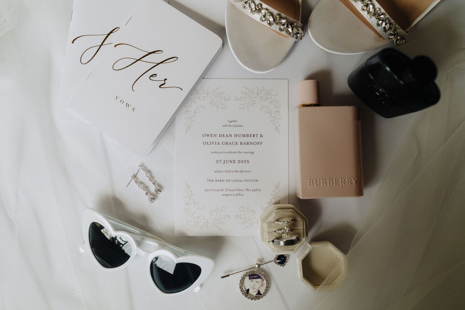 Wedding invitation and details flatlay with sunglasses, shoes, and perfume on white background.