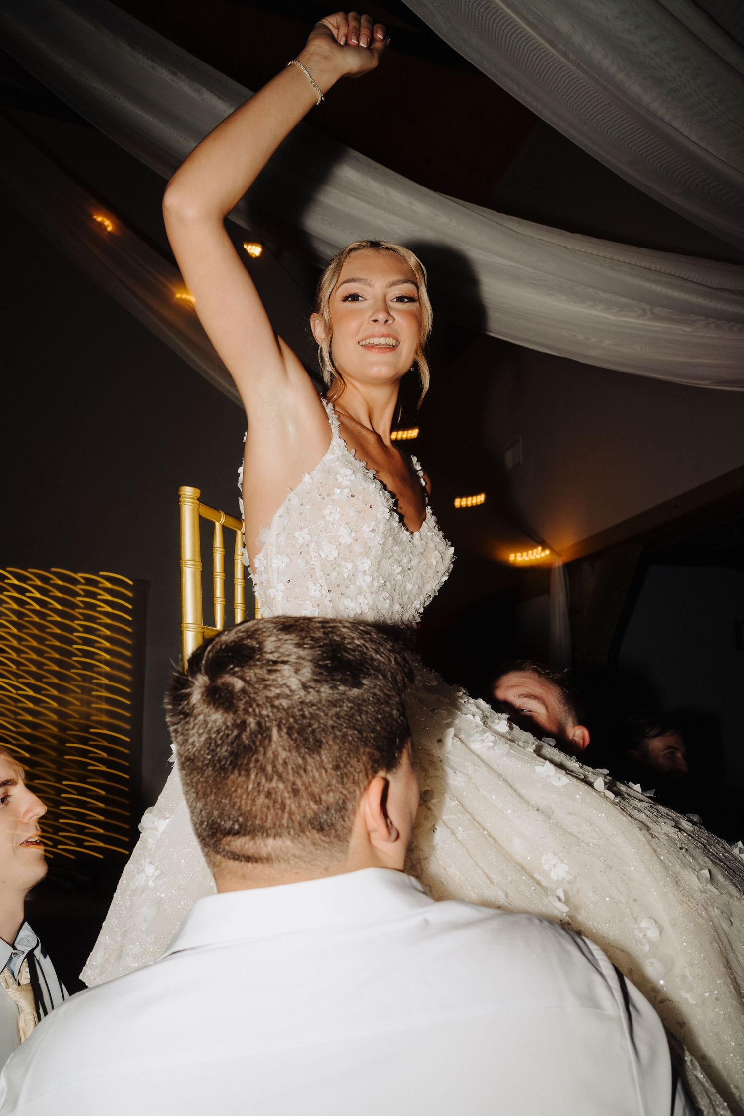 Wedding reception dance floor moments captured in dramatic lighting under draped fabric ceiling.