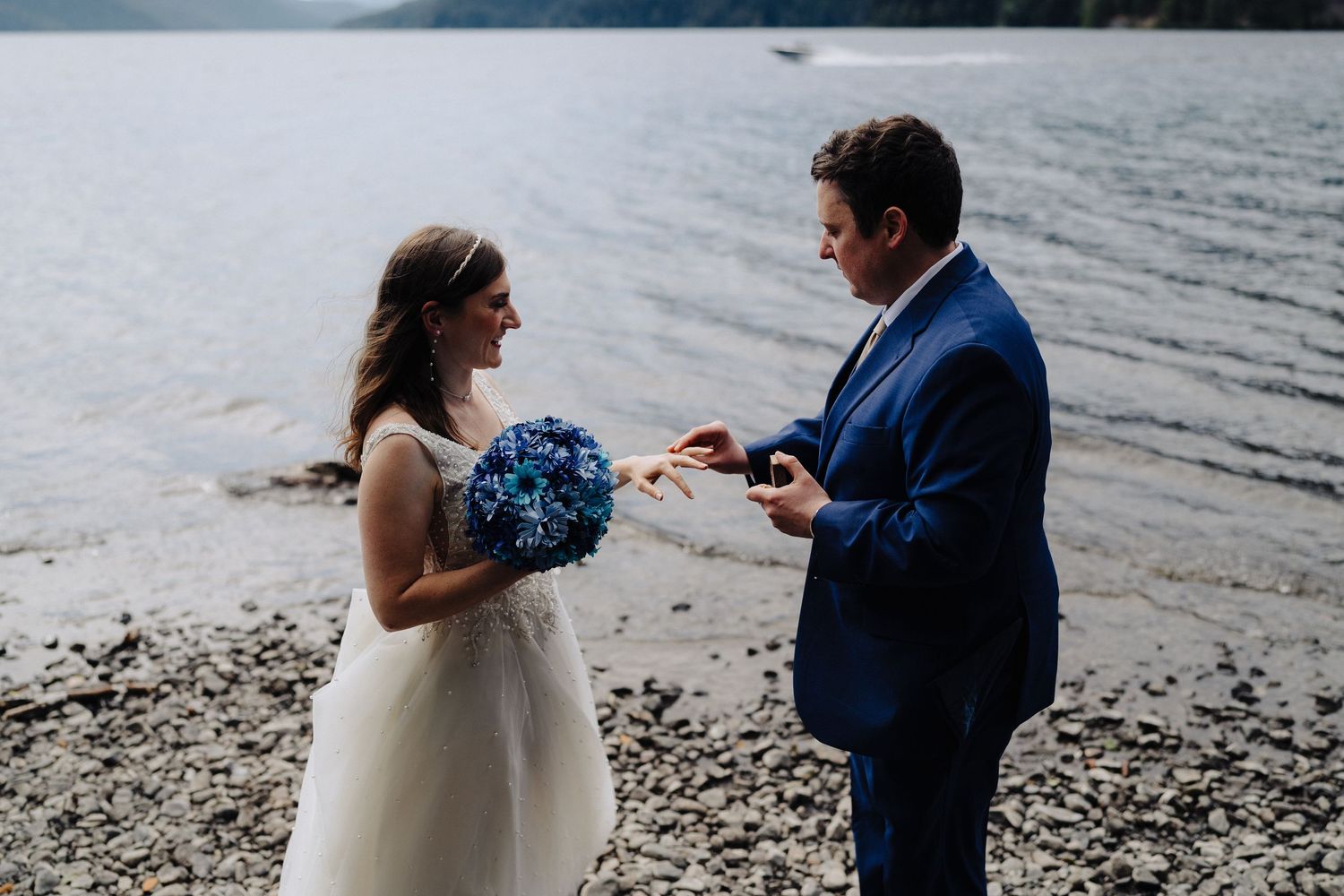 A wedding proposal scene on a rocky beach with a blue bouquet and navy suit.