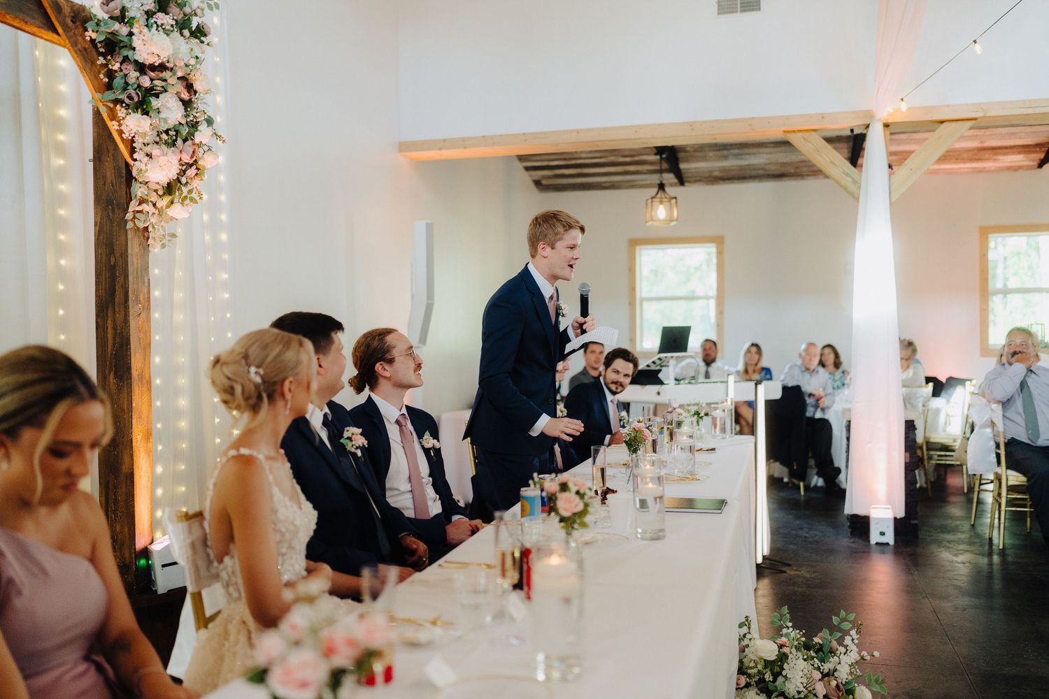 Modern white wedding reception venue with elegant table settings and string lights.