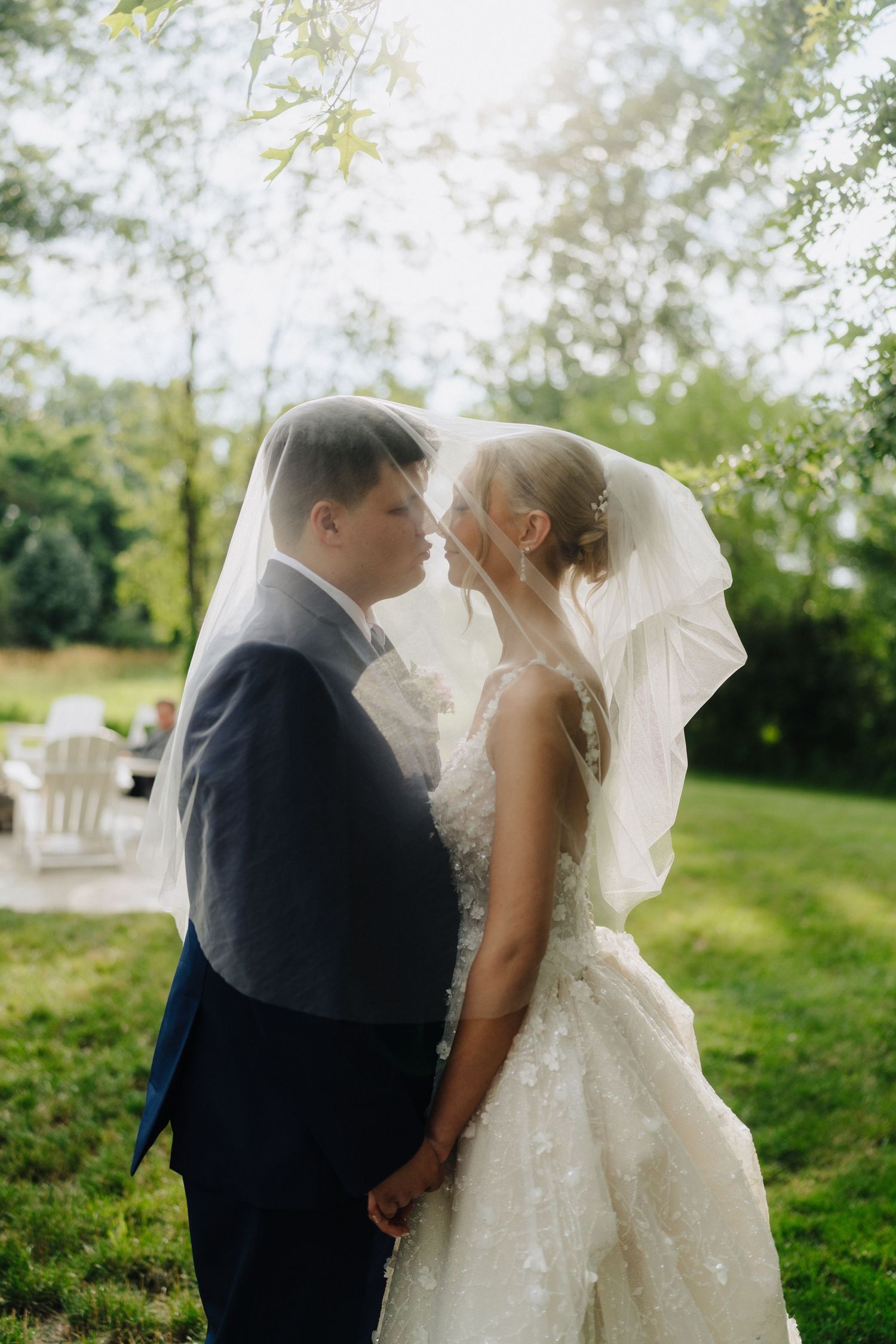 A romantic wedding couple shares intimate moments under a flowing veil in a lush green garden setting.