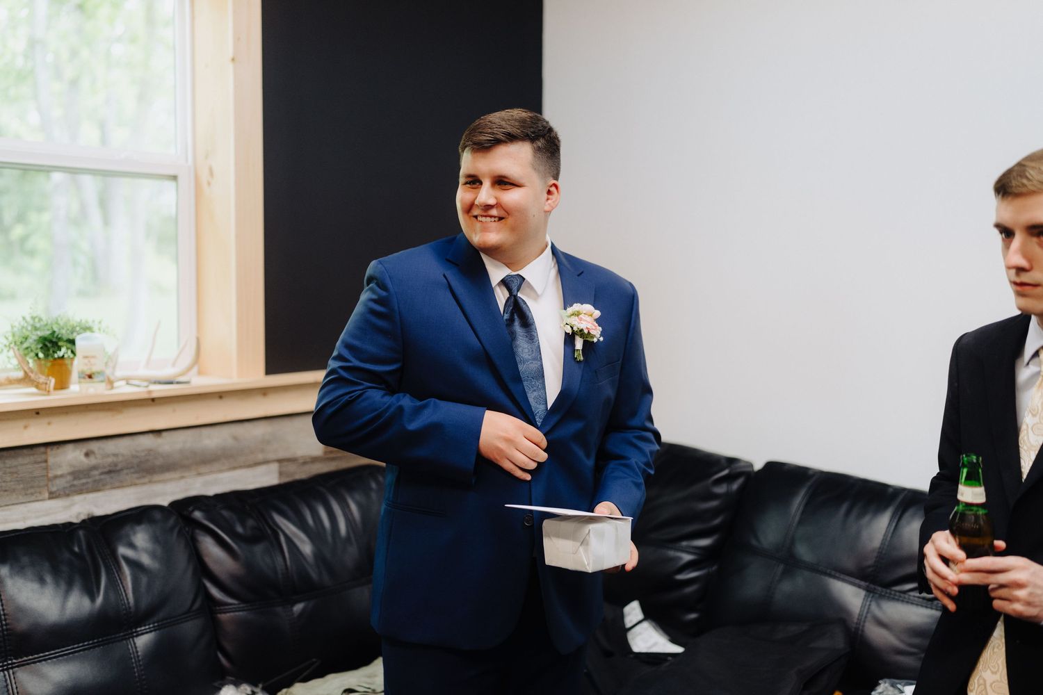 Groomsmen in navy suits gather together while reading letters in a brightly lit room.
