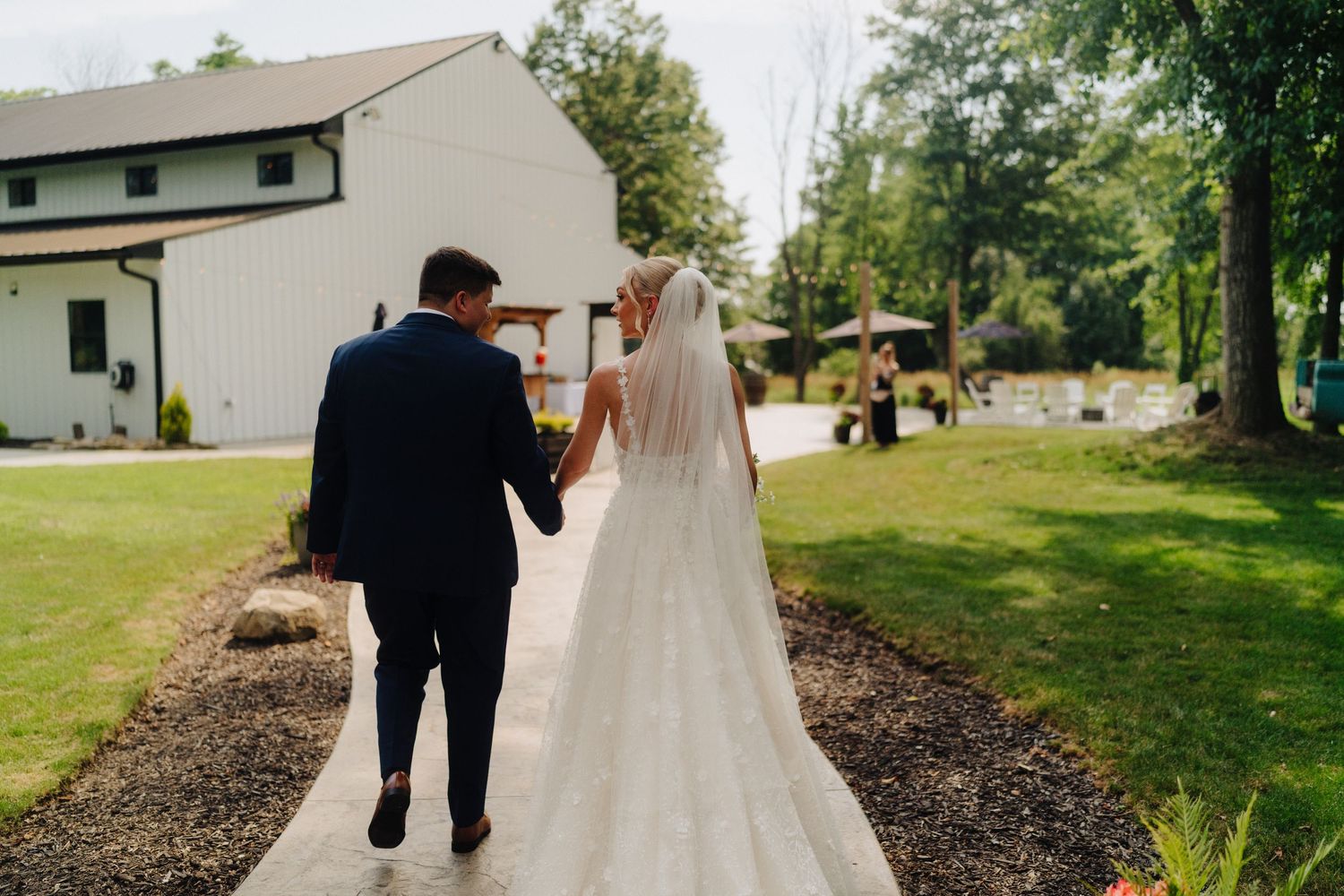 Newlyweds walking away on garden path with bride's long veil trailing behind.