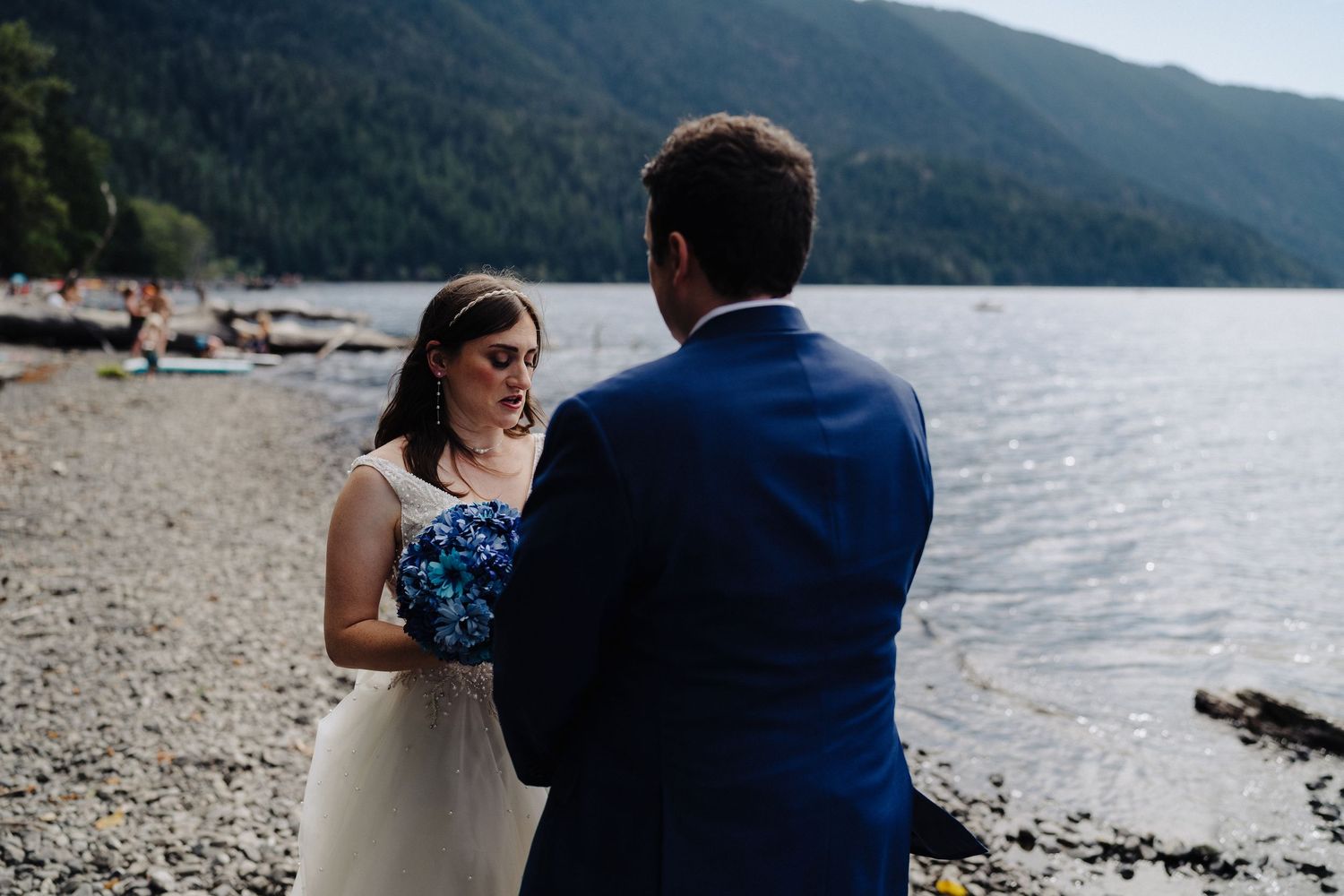 A wedding ceremony takes place on a scenic mountain lake shore with a rocky beach.