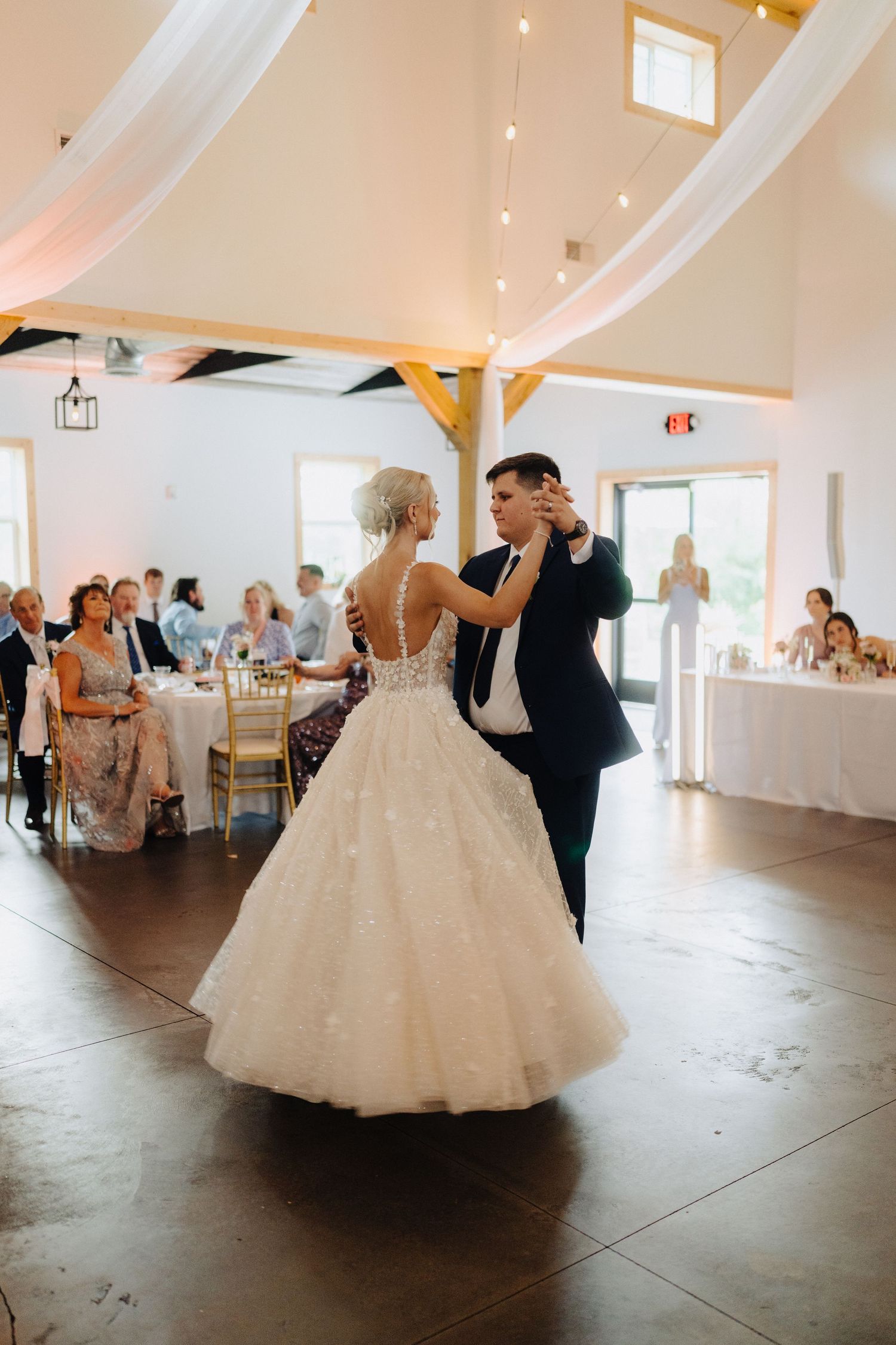 Wedding couple sharing their first dance in a bright, white-decorated reception venue.
