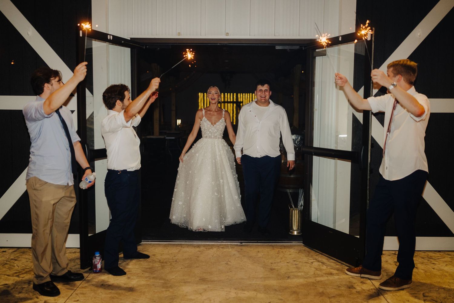 Wedding reception guests dancing and celebrating in a rustic white venue.