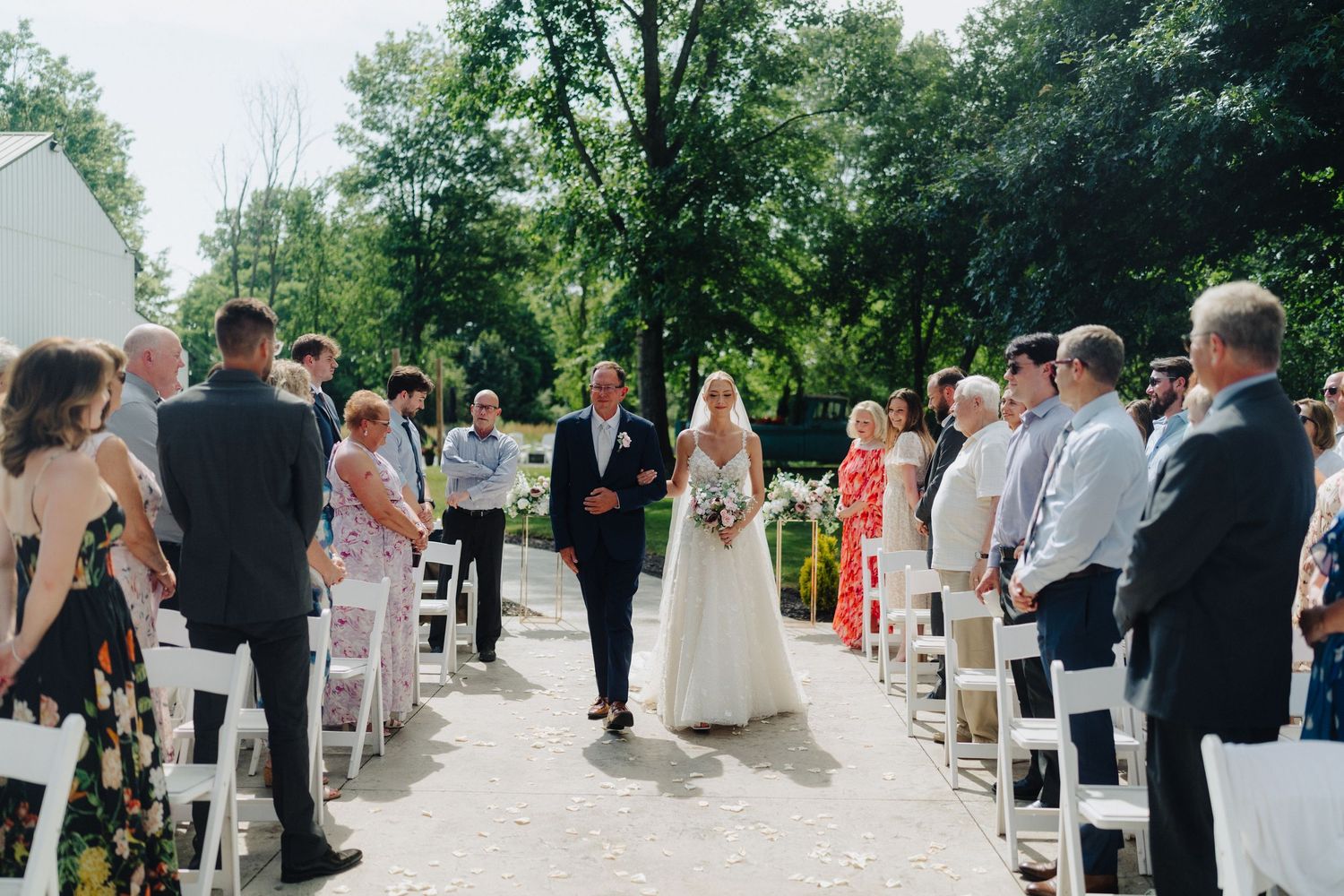 Wedding guests gathered for outdoor ceremony with white chairs and natural setting.