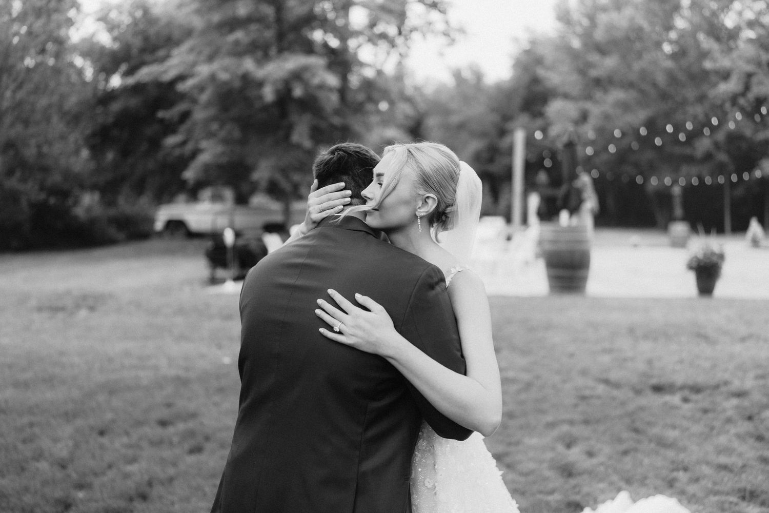 A tender embrace between newlyweds in black and white during an outdoor wedding reception.