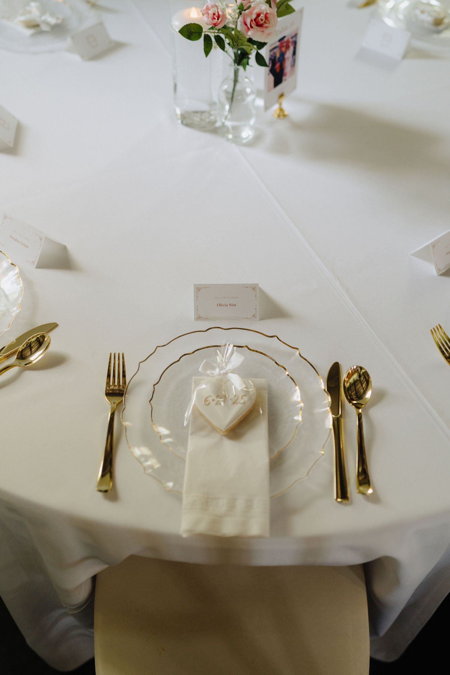 Elegant wedding table setting with white linens, gold cutlery, and pink rose centerpieces.
