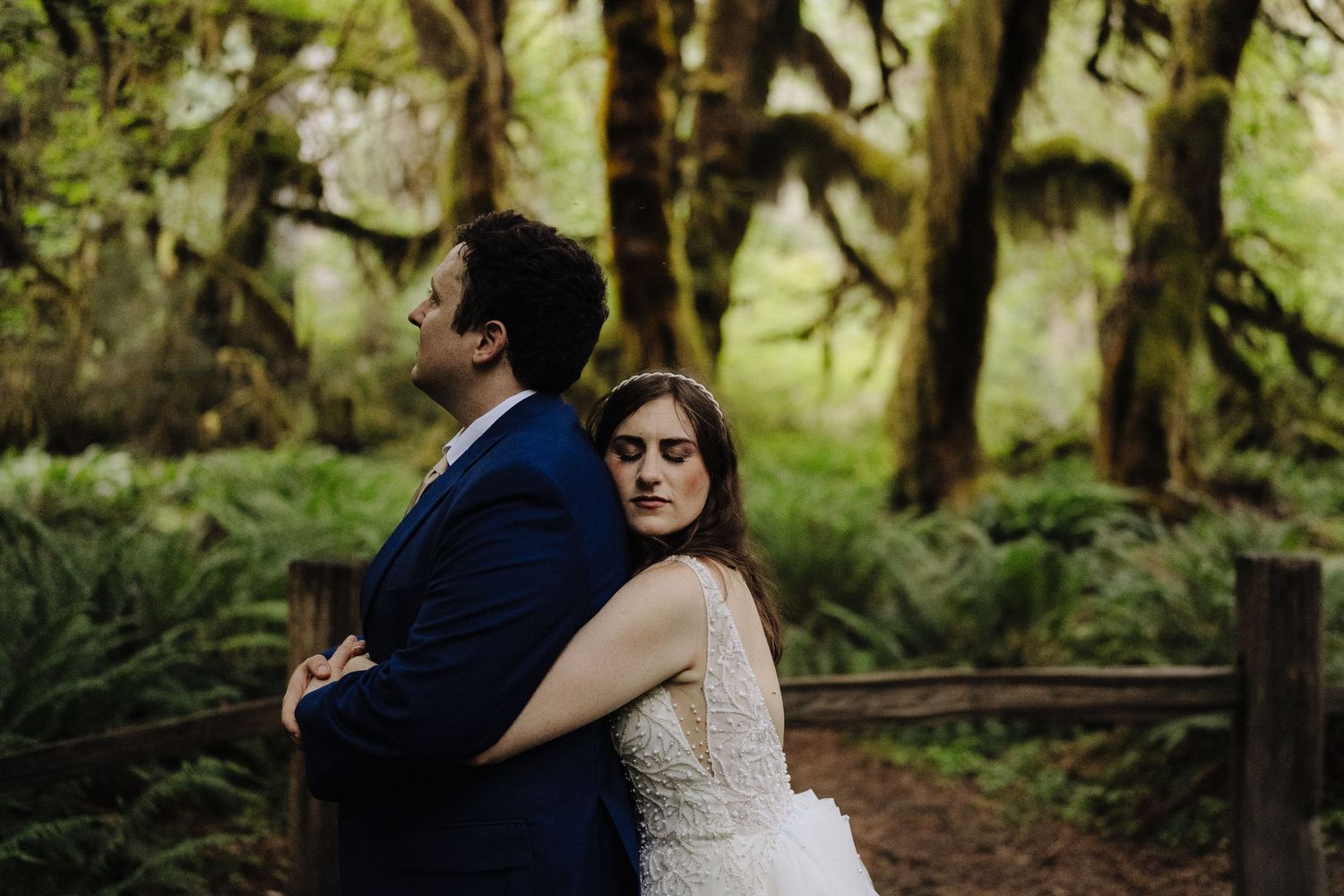 A couple embraces in a lush green forest setting during their wedding photoshoot.