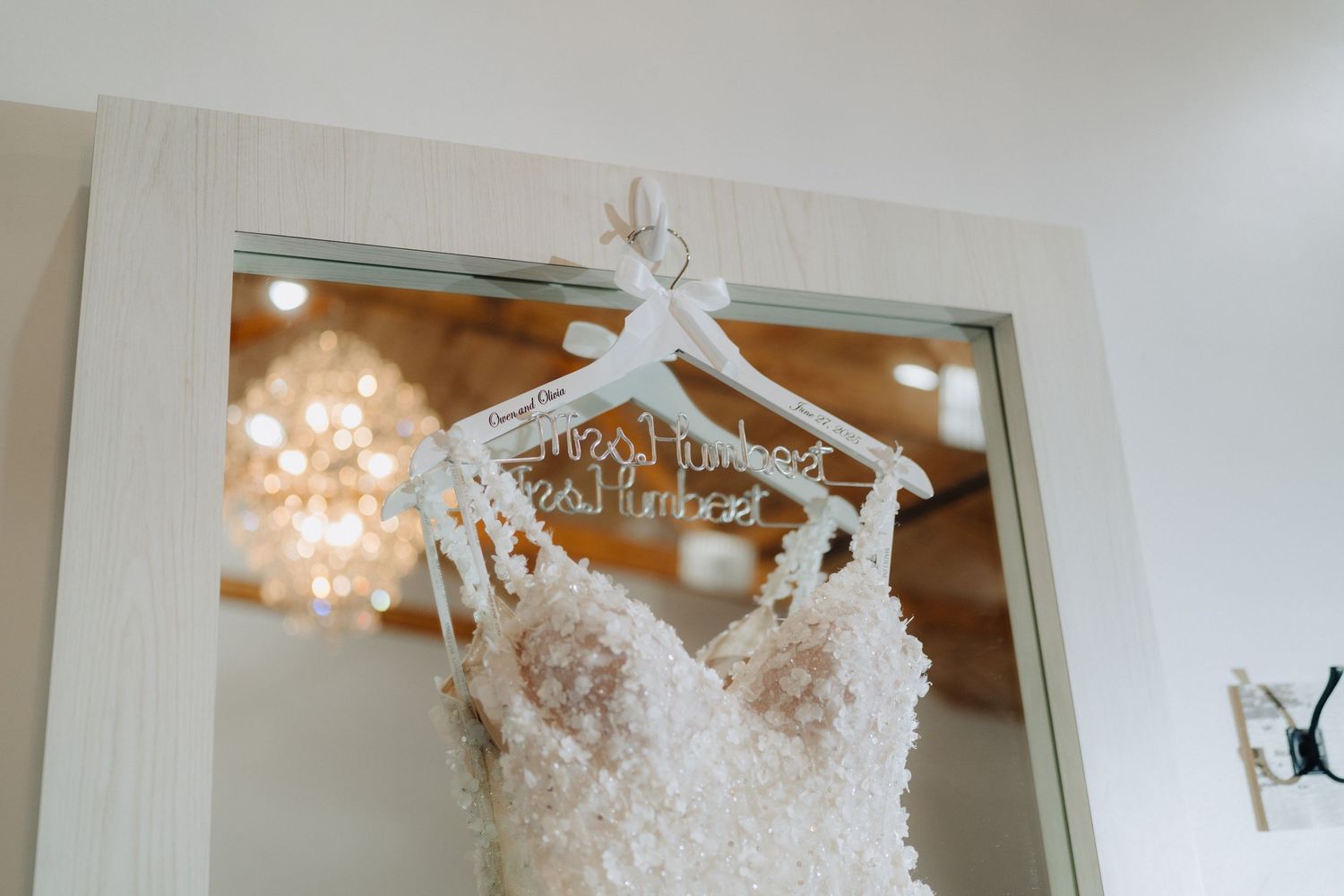 A wedding dress hangs elegantly in a brightly lit room with crystal chandeliers.