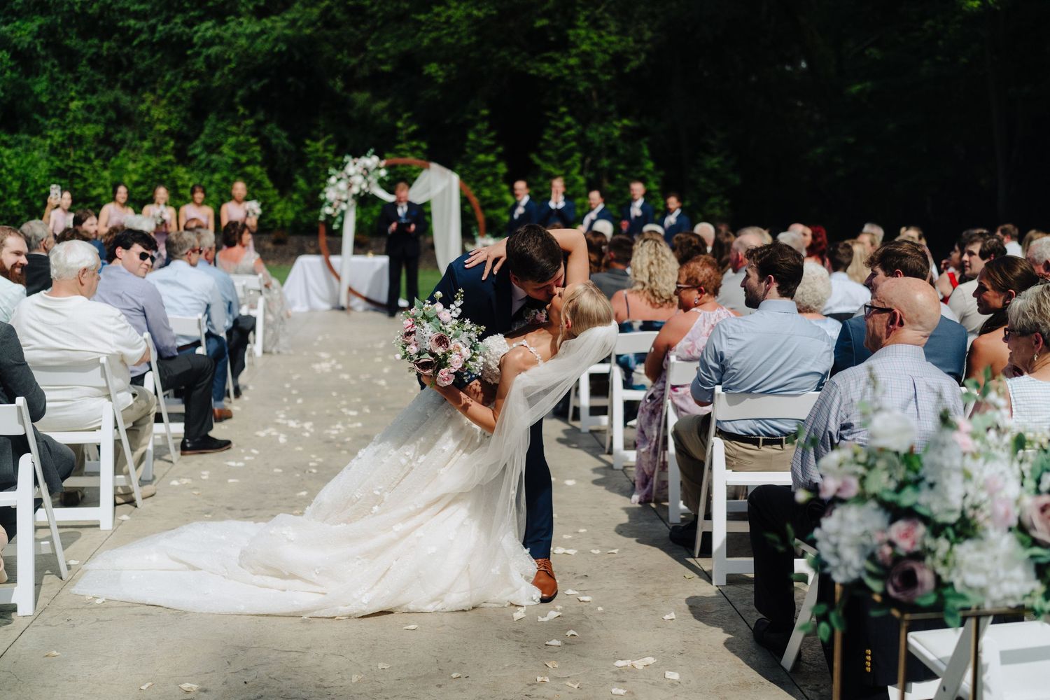 Wedding ceremony recessional with guests seated on white chairs outdoors.