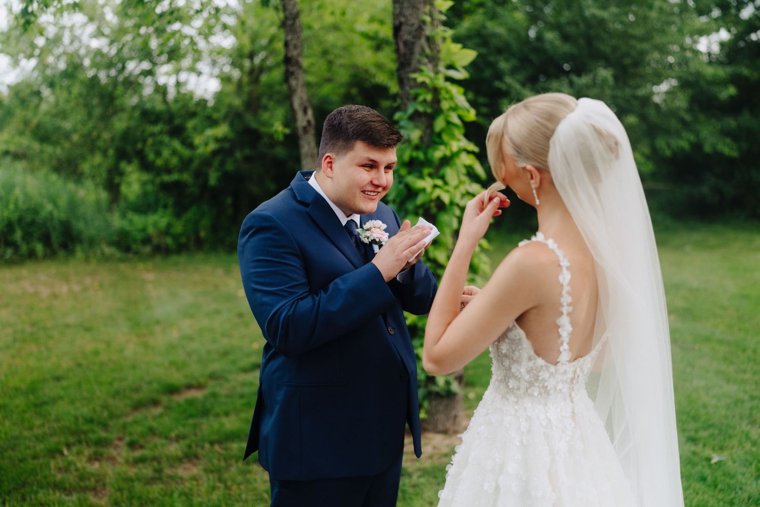 First look moment between couple in navy suit and white wedding dress in outdoor garden setting.