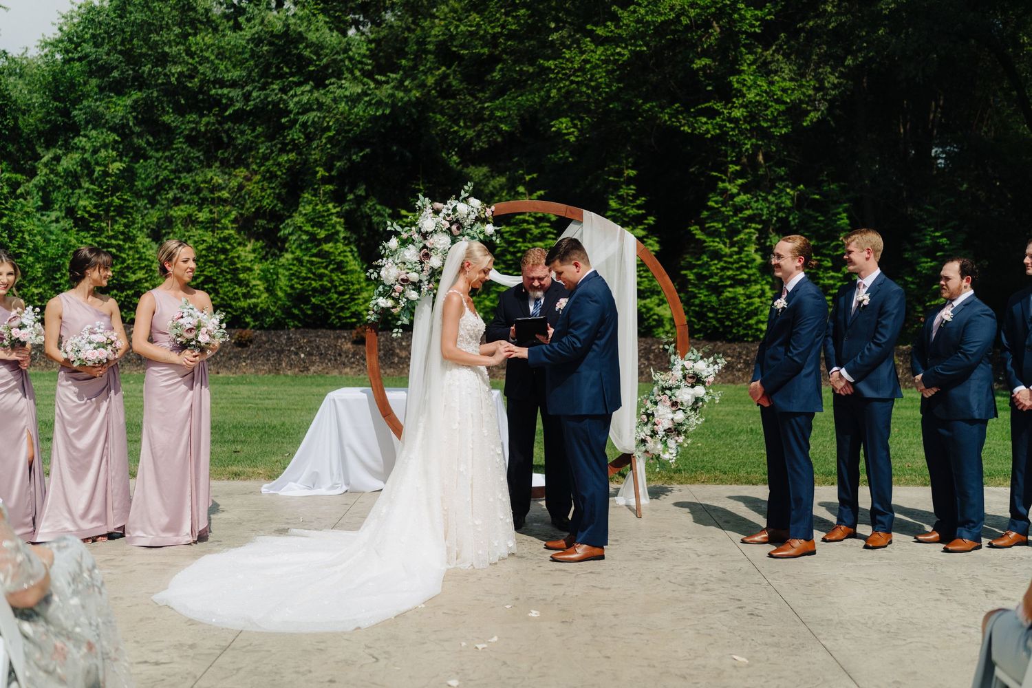 Wedding party and guests arranged for formal ceremony photos outdoors.