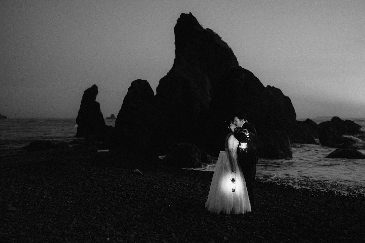 Ethereal silhouette of couple illuminated against dramatic coastal rock formations at dusk.