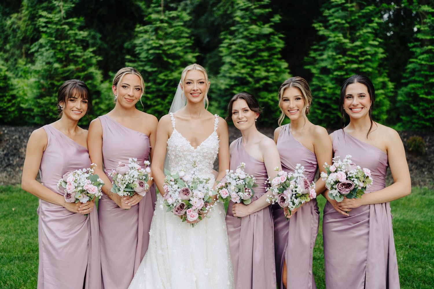 Bridesmaids wearing matching mauve dresses pose together in a garden setting.