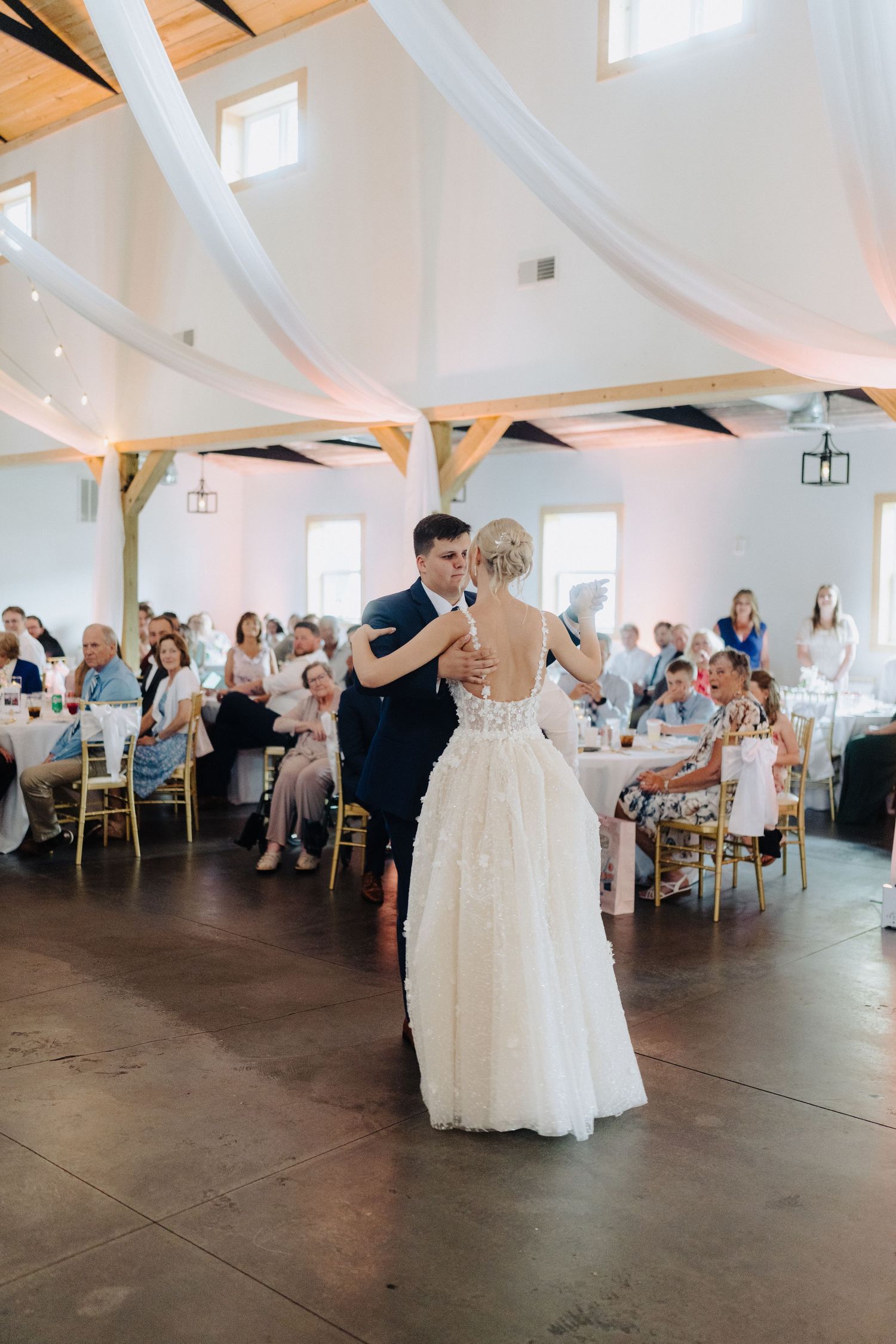 A sequence of photos showing a romantic first dance at a wedding reception in a bright, white-decorated venue.