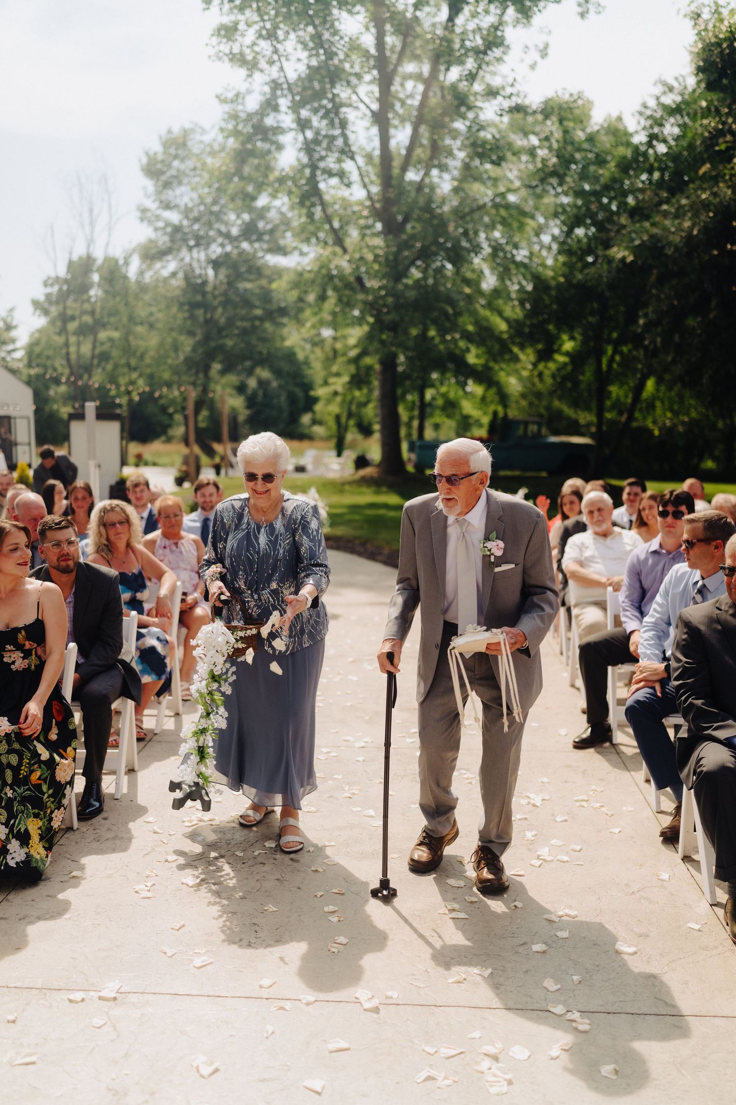 Wedding guests line up outside on a sunny day throwing flower petals during an outdoor celebration.