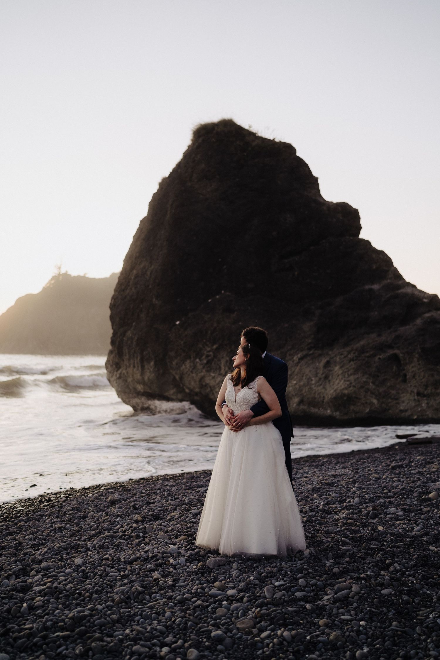 Sunset wedding portrait with dramatic black rock formations and ocean waves.