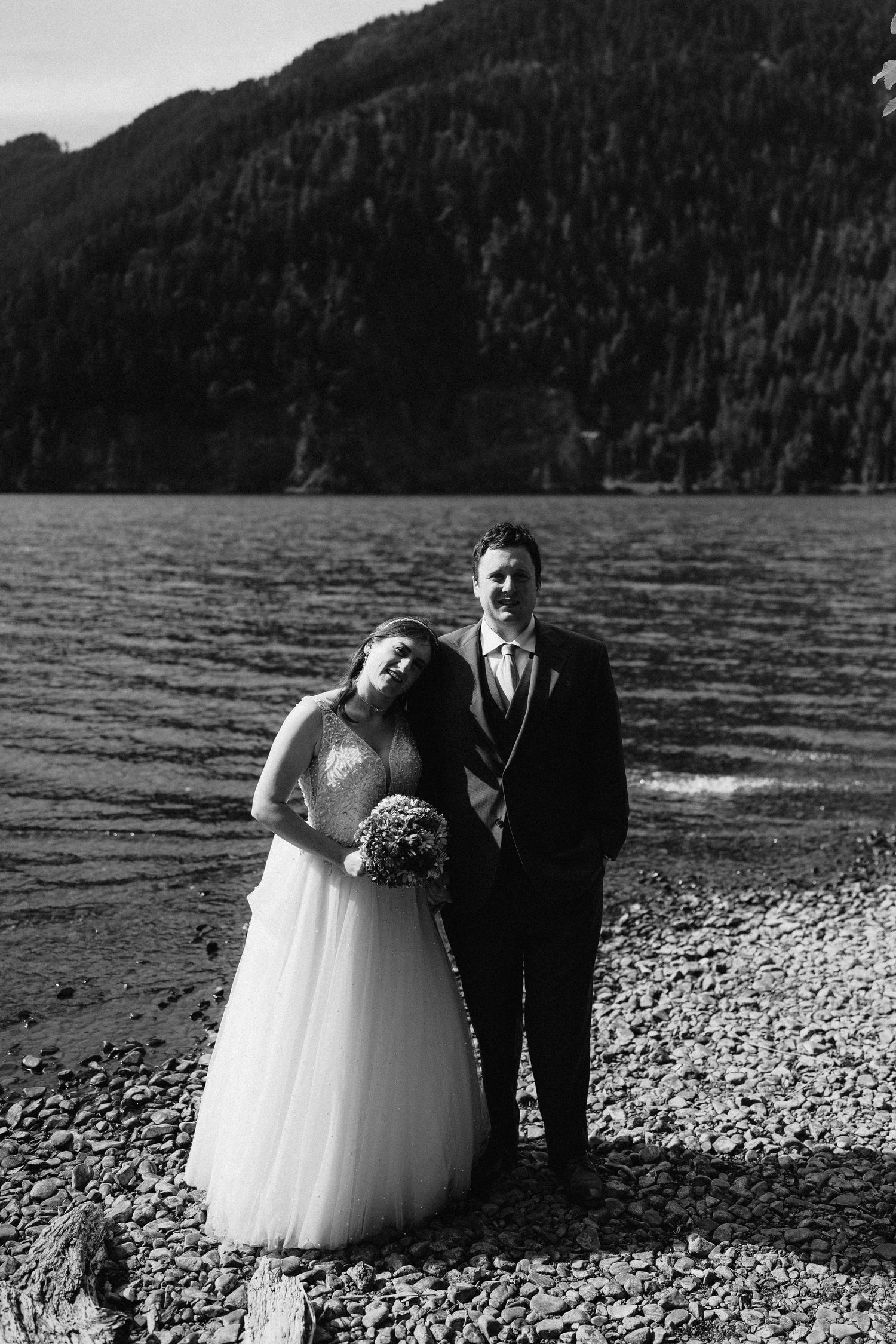 Black and white wedding photo of a couple on a scenic mountain lake shore.
