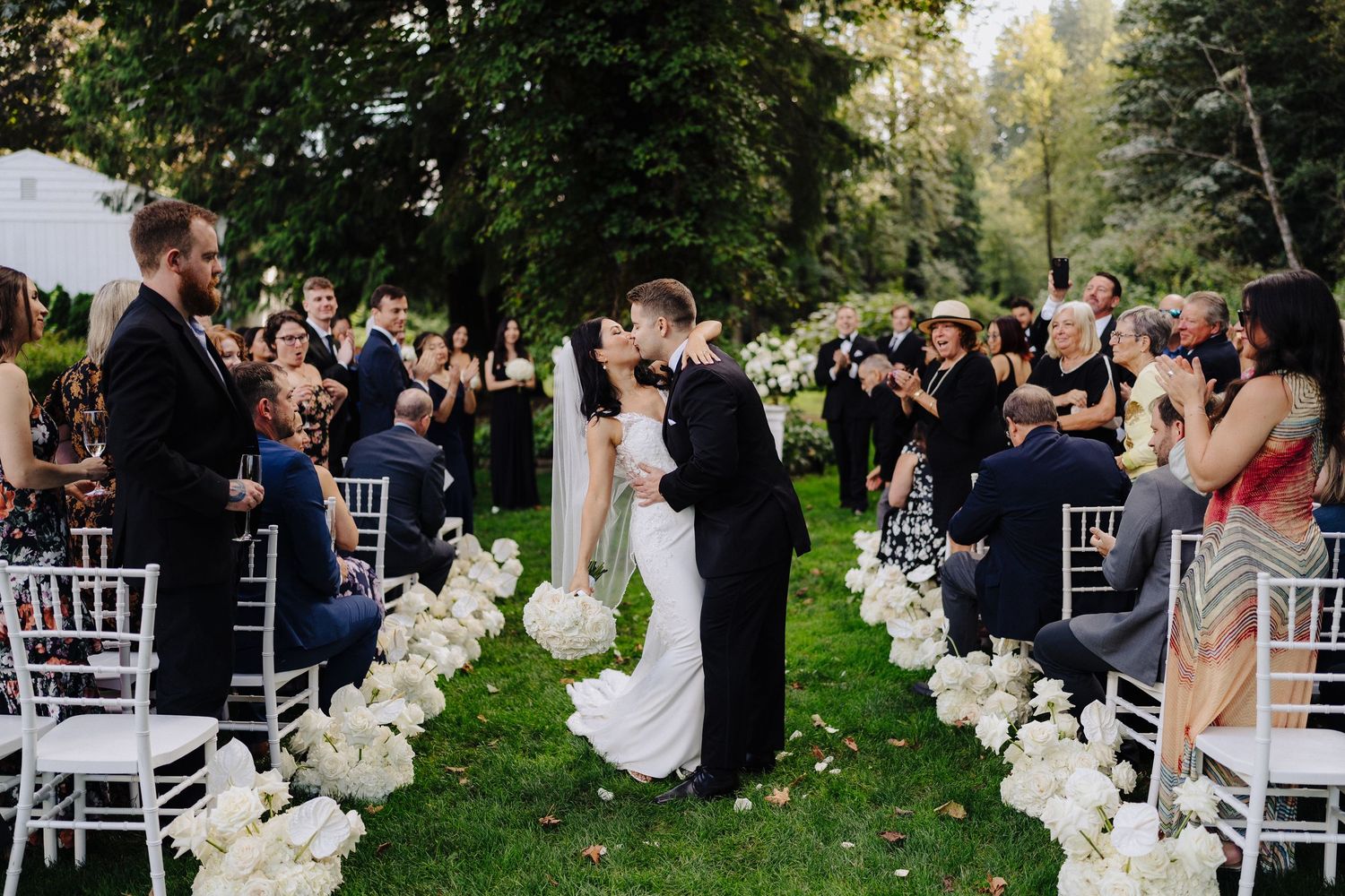 Outdoor garden wedding ceremony with white floral aisle decorations.