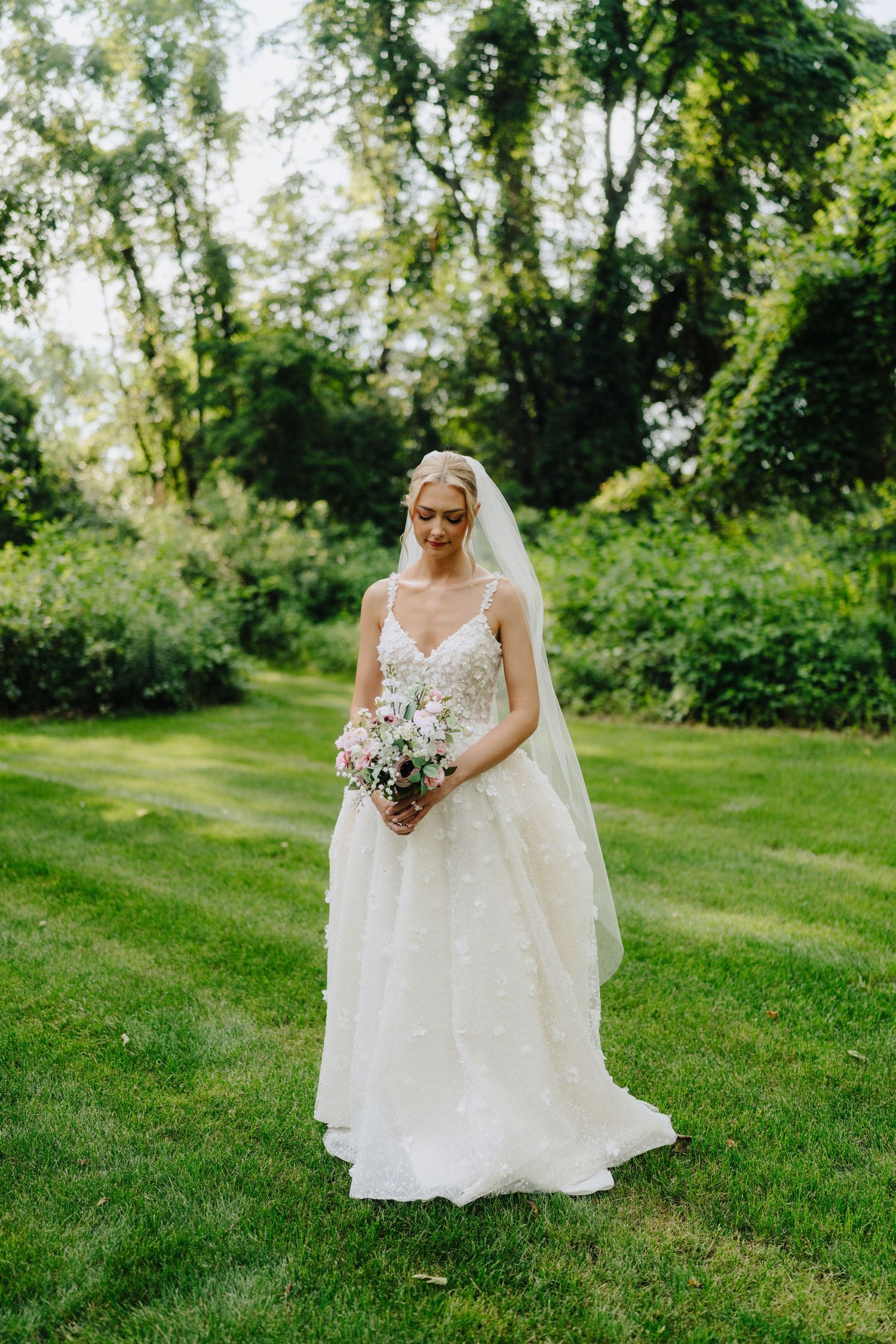 Bride in an elegant lace wedding dress poses in a sunlit garden setting.