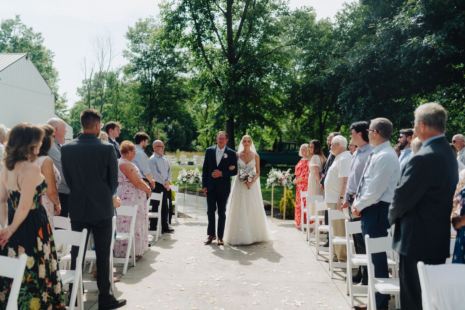 An outdoor wedding ceremony with white chairs and guests in formal attire.