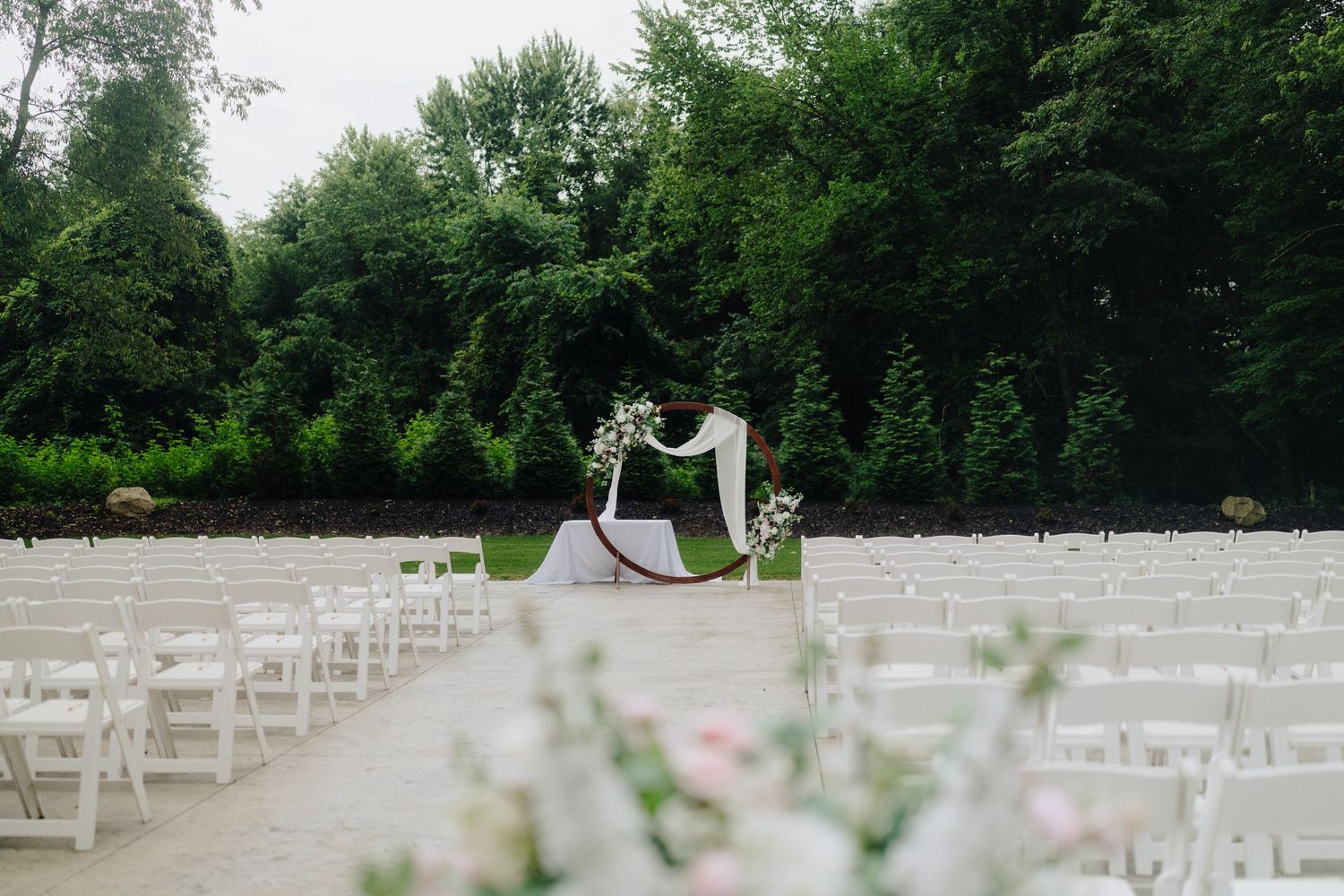 White wedding ceremony chairs arranged in rows on a grassy lawn with trees in background.