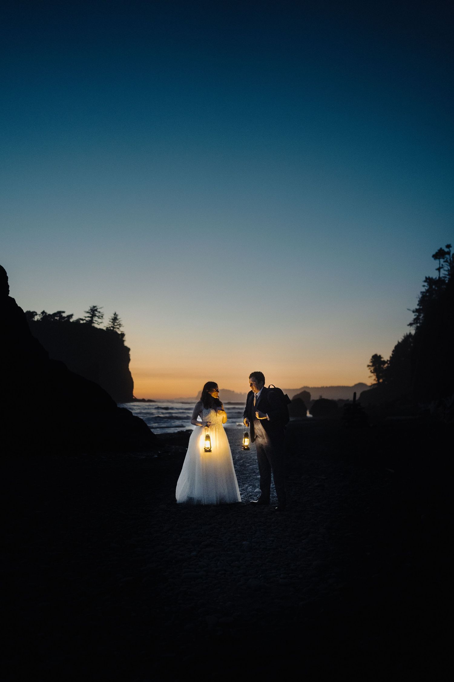 Romantic wedding portrait with couple in silhouette against sunset on dramatic beach landscape.
