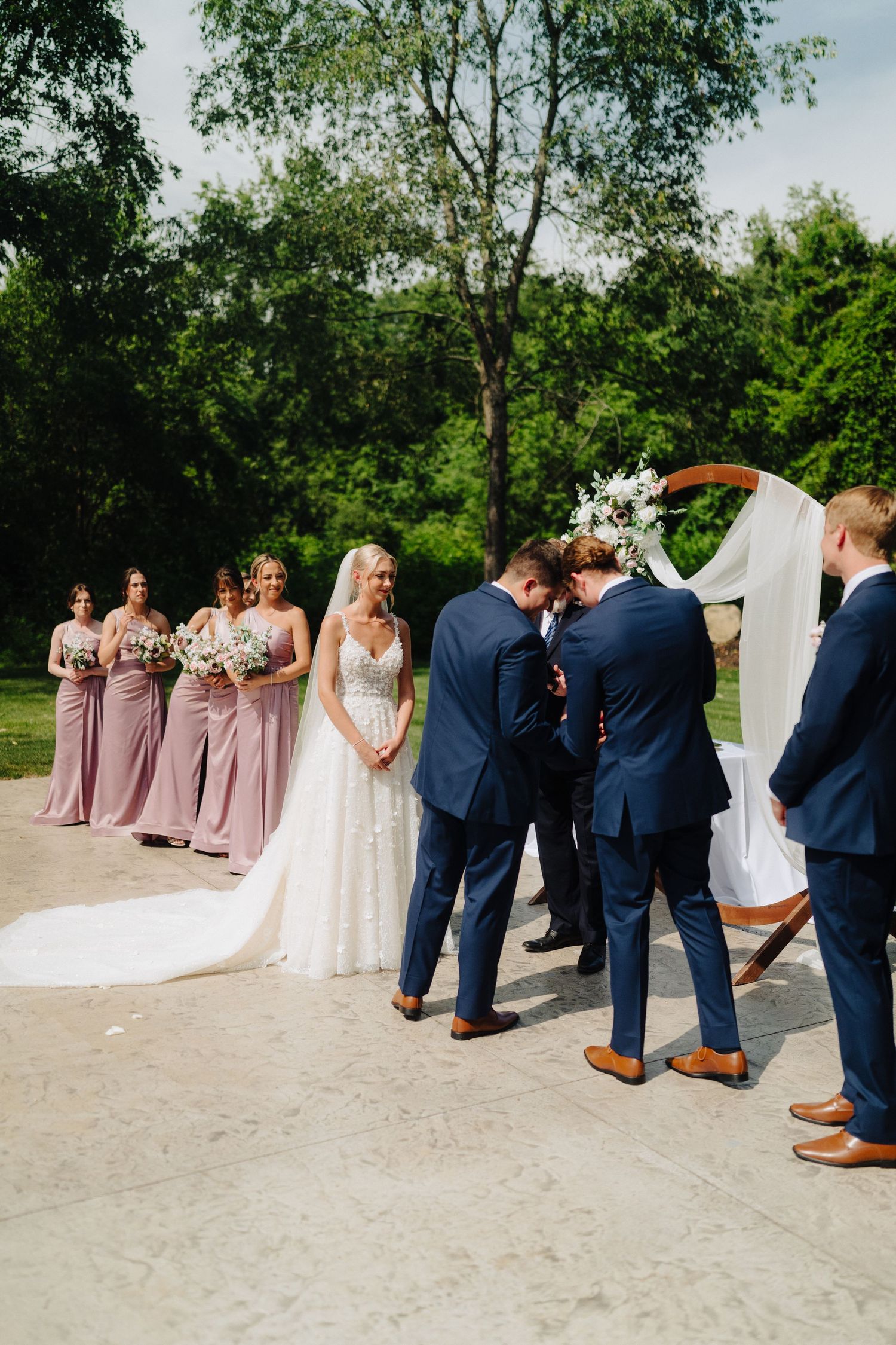 Wedding ceremony with bridal party in mauve dresses and groomsmen in navy suits.