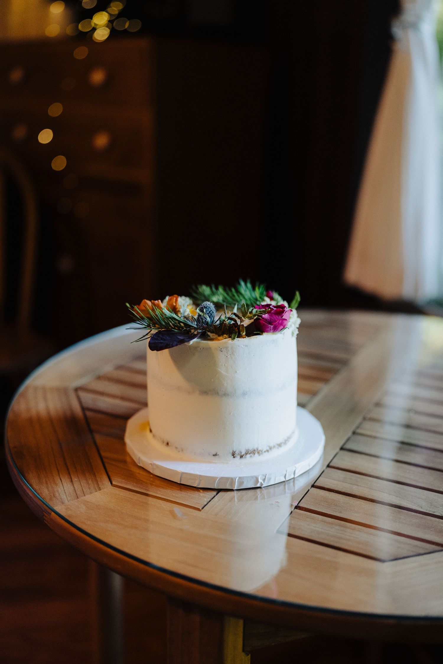 A white wedding cake decorated with fresh succulents and flowers sits on a wooden table.
