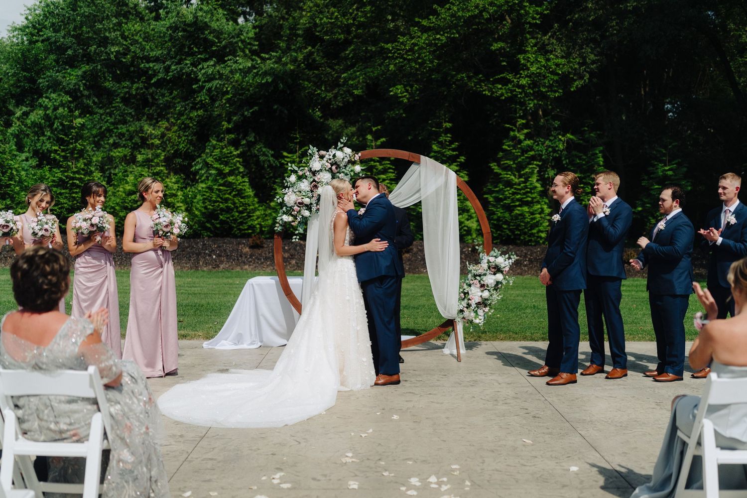 Wedding party and guests lined up for outdoor ceremony against natural backdrop.