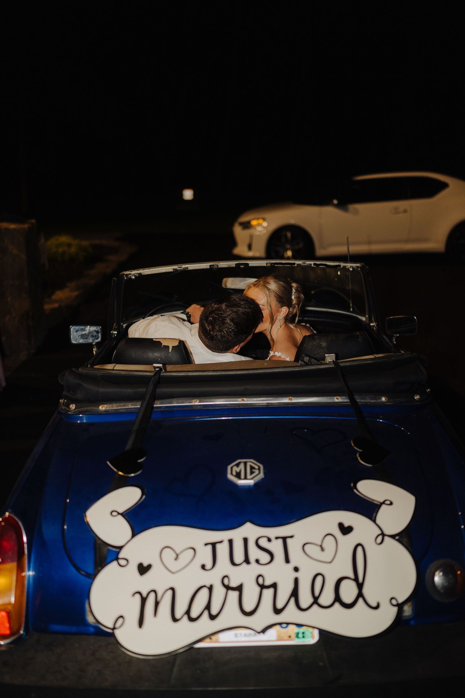 A blue vintage car decorated with 'Just Married' signage parked at night.