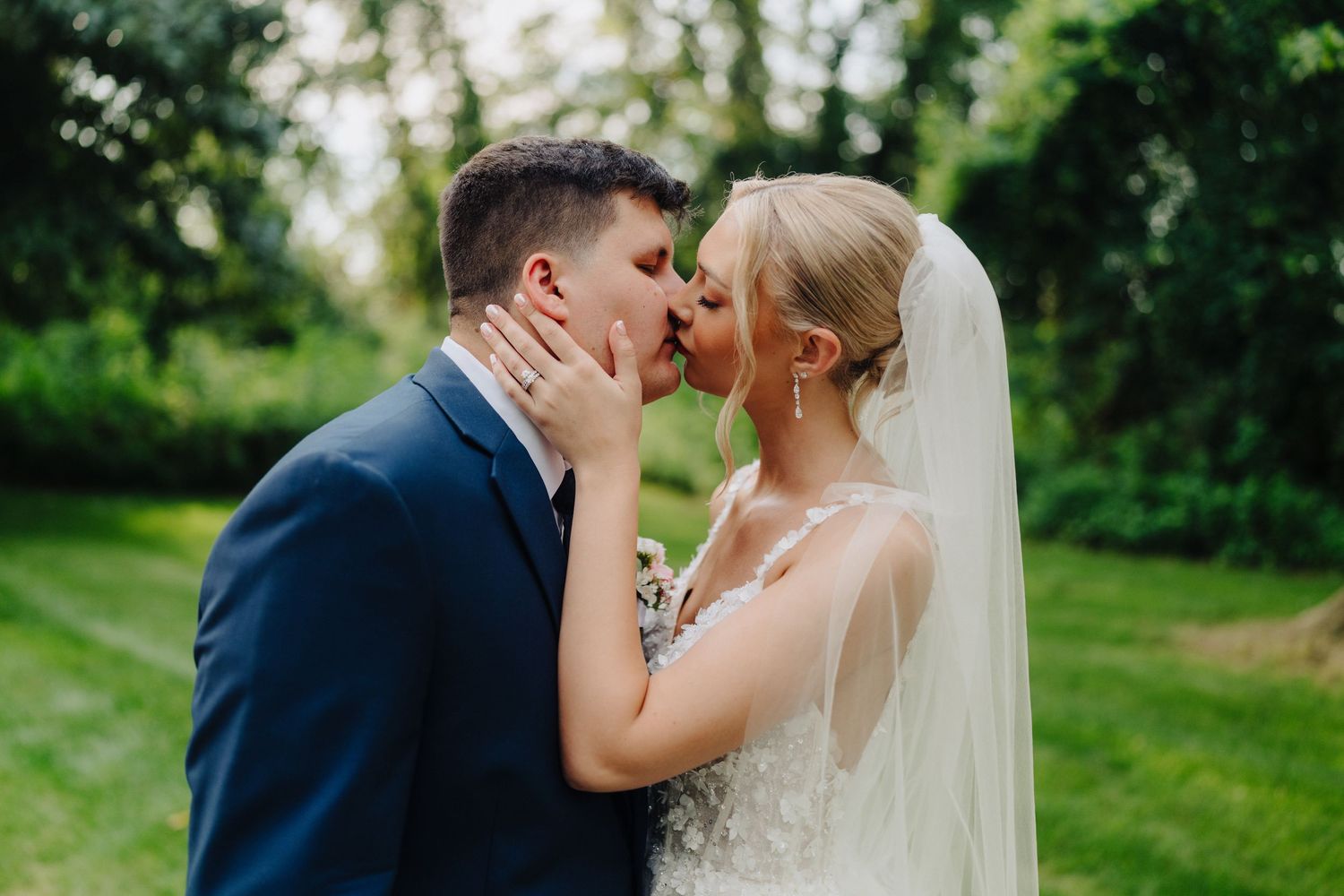 Intimate wedding couple portrait with flowing veil in outdoor garden setting.