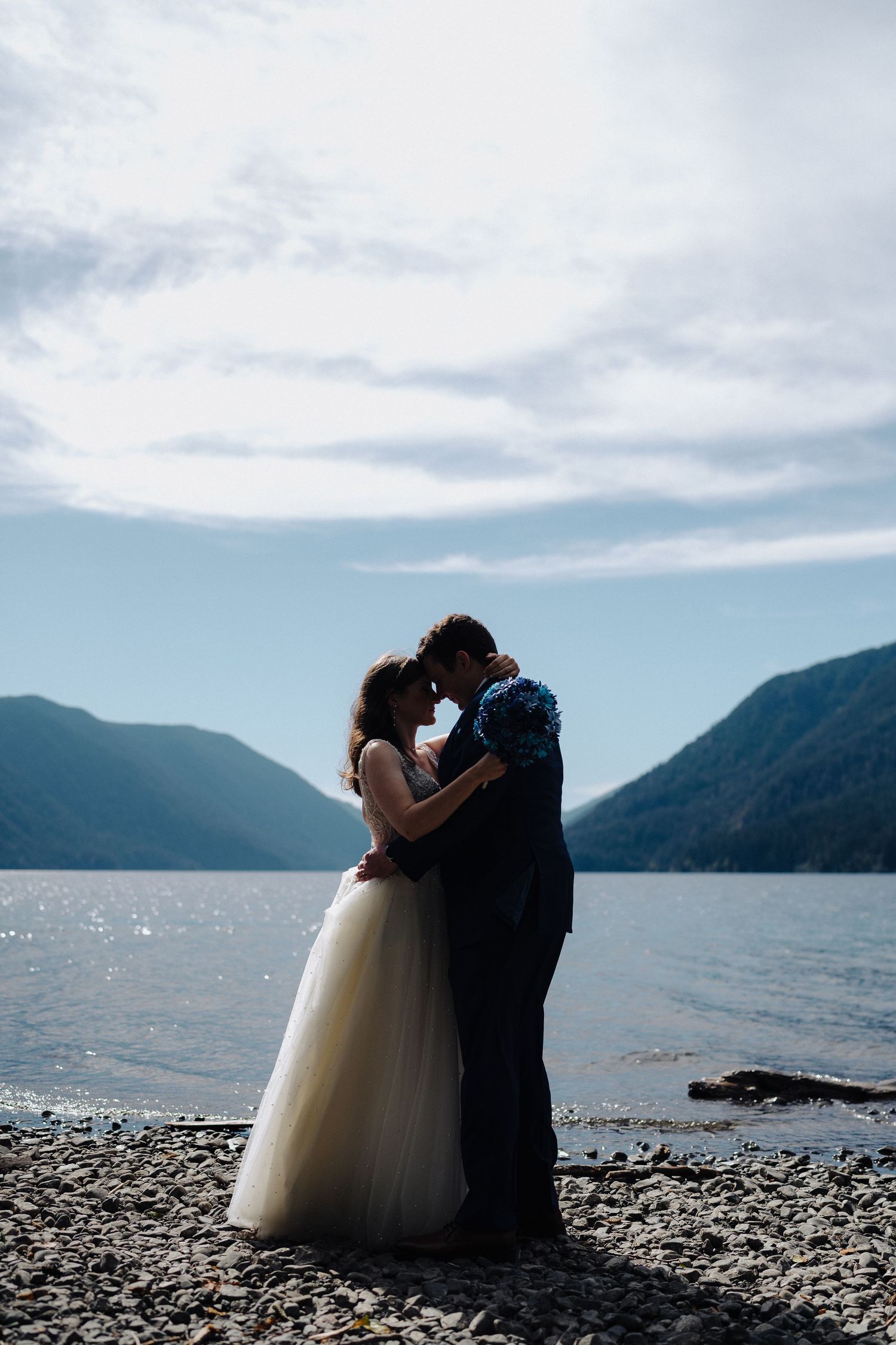 Intimate wedding photos captured against backdrop of lake and mountains on overcast day.