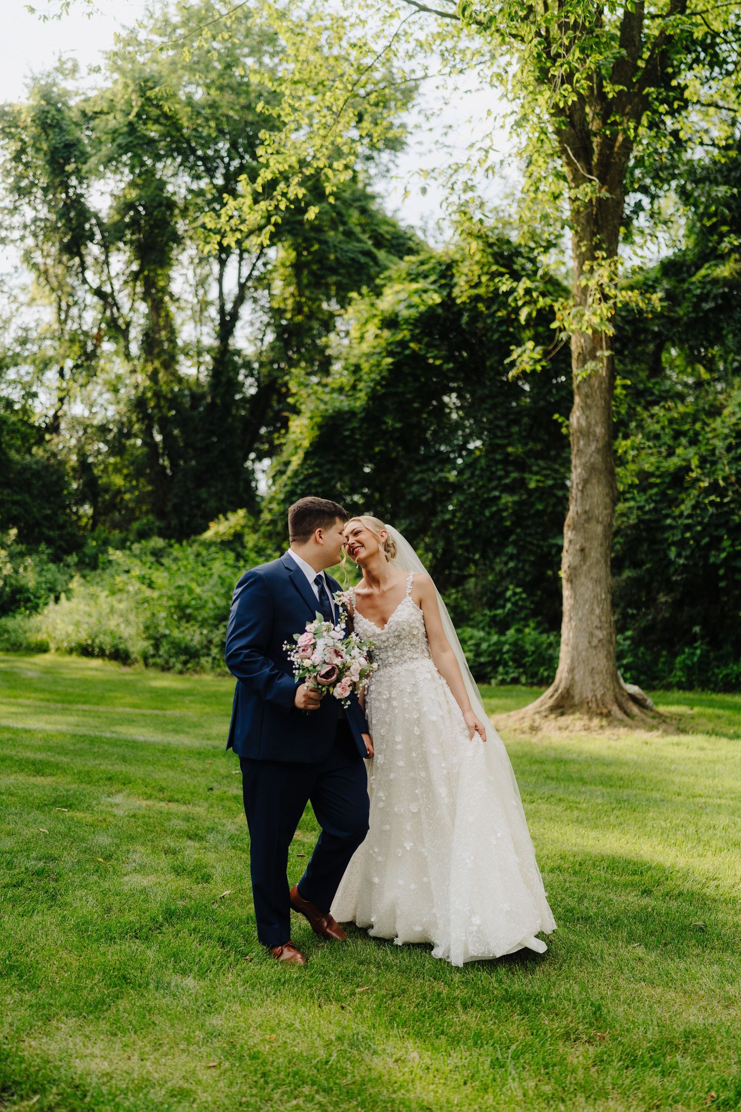 Wedding couple walks hand in hand through a scenic garden path with tall trees.