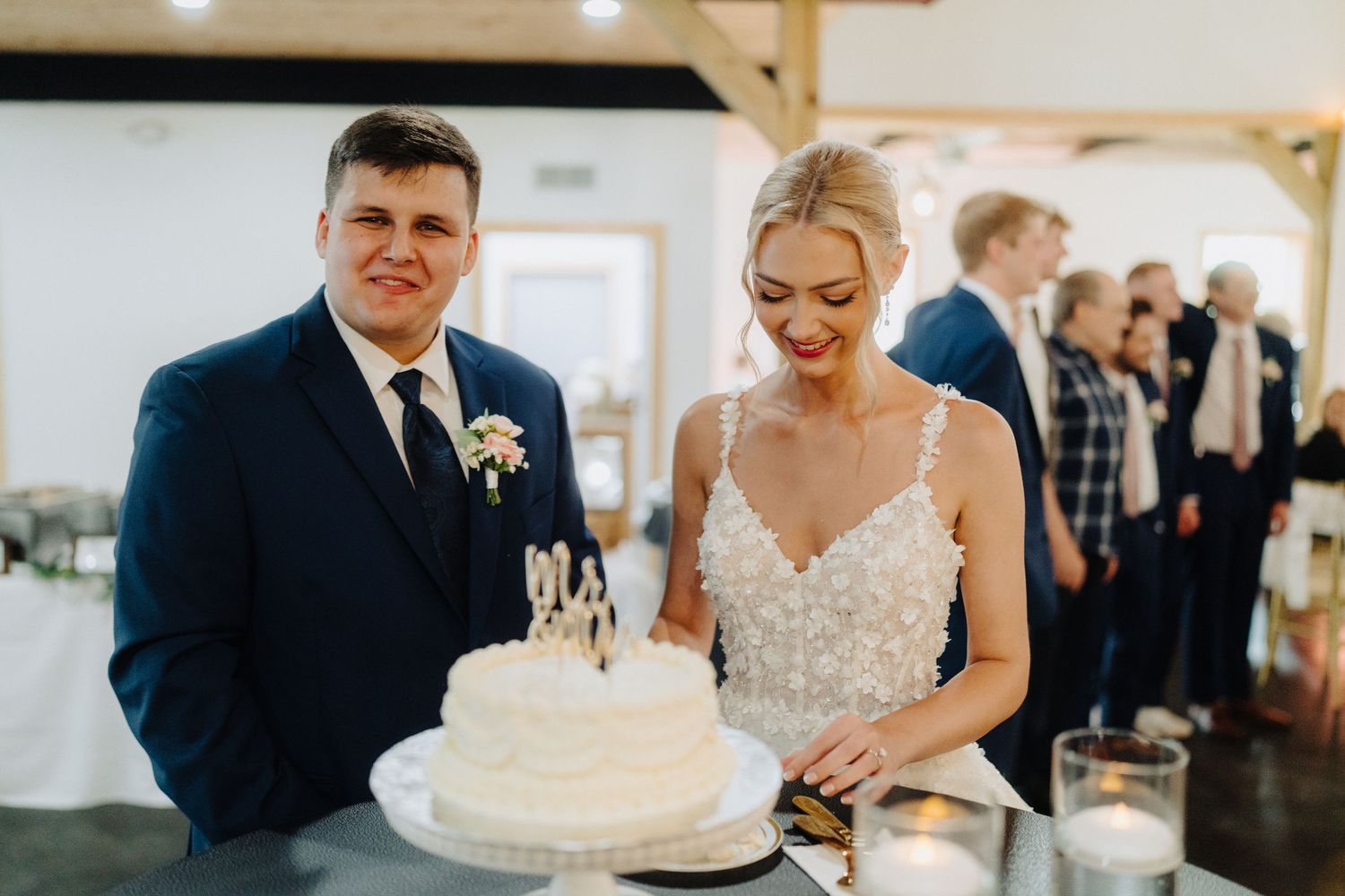 Wedding party gathered around a white tiered cake during the reception celebration.