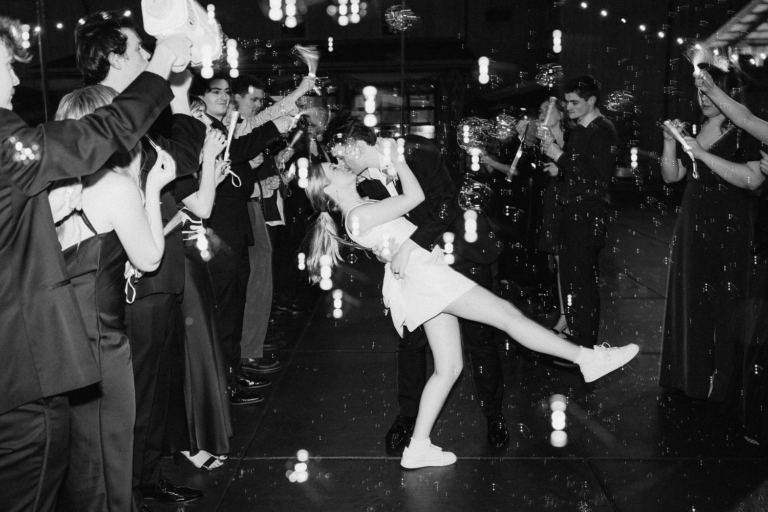 Wedding guests dance and celebrate in a dimly lit venue with string lights overhead.