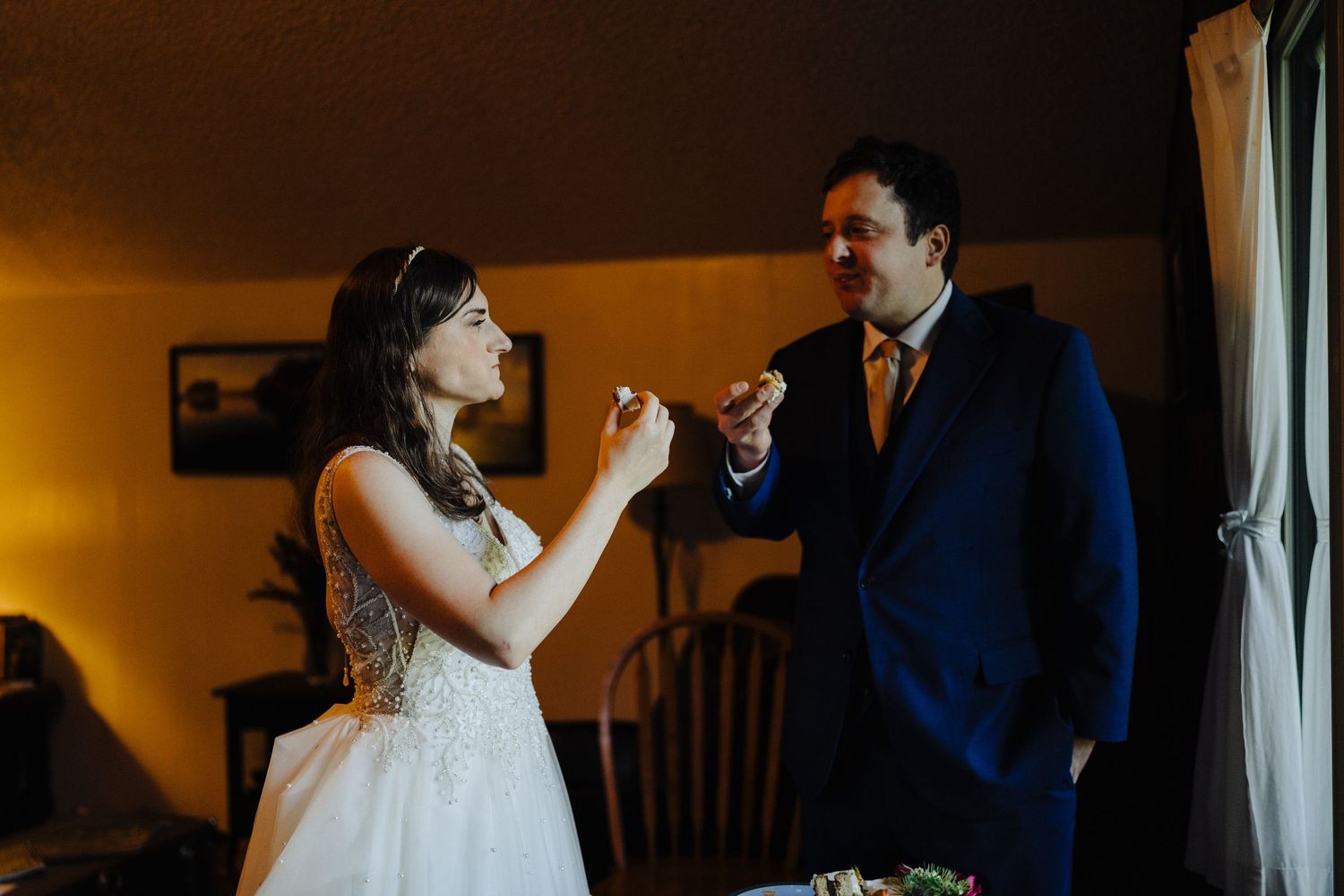 Wedding couple sharing playful moment in warmly lit indoor setting.