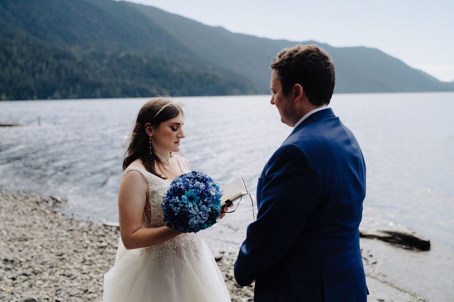 Romantic wedding couple embraces along a scenic mountain lake shoreline.