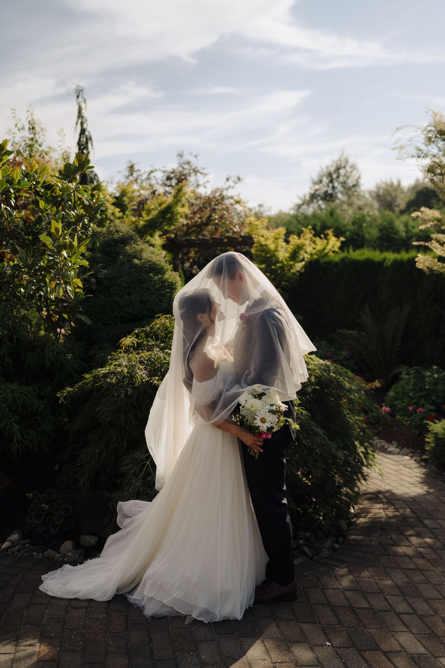 Romantic garden wedding moment with bride's veil flowing in sunlit outdoor setting.